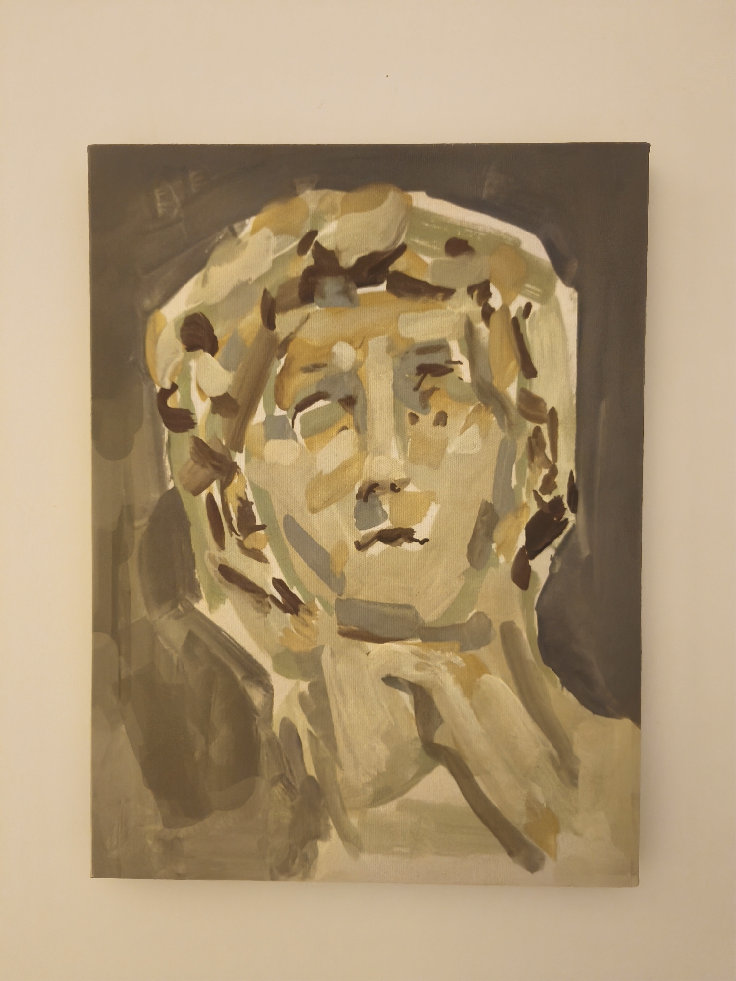 The image shows a painting of a bust of a person. The painting is rendered in a loose, impressionistic style with broad brushstrokes and a muted color palette dominated by shades of brown, beige, and gray. The subject's face is central, with abstract representations of features. The body is also depicted abstractly, with the neck and shoulders visible. The background is a dark, muted gray. The painting is on a canvas and is hung on a plain, cream-colored wall. The overall impression is a classical subject rendered in a modern, painterly style. There is no discernible information in the image that would allow for the identification of a specific location in Yerevan, Armenia.