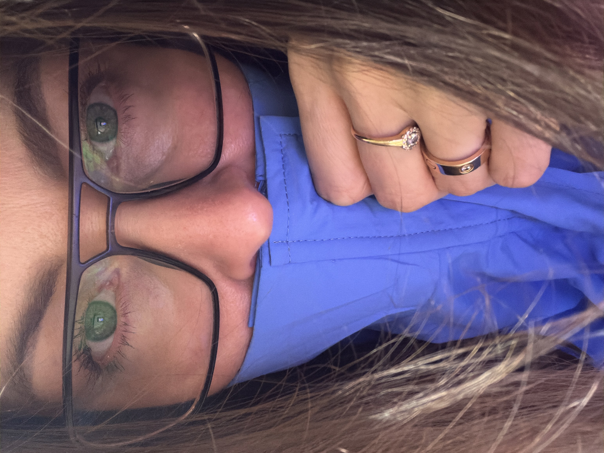 A close-up, rotated image shows a person wearing glasses, a blue collared shirt, and two rings on their finger. The person's eyes are visible through the glasses. Hair frames the edges of the image. The location in the city of Markovo, Russia is not indicated in the image.