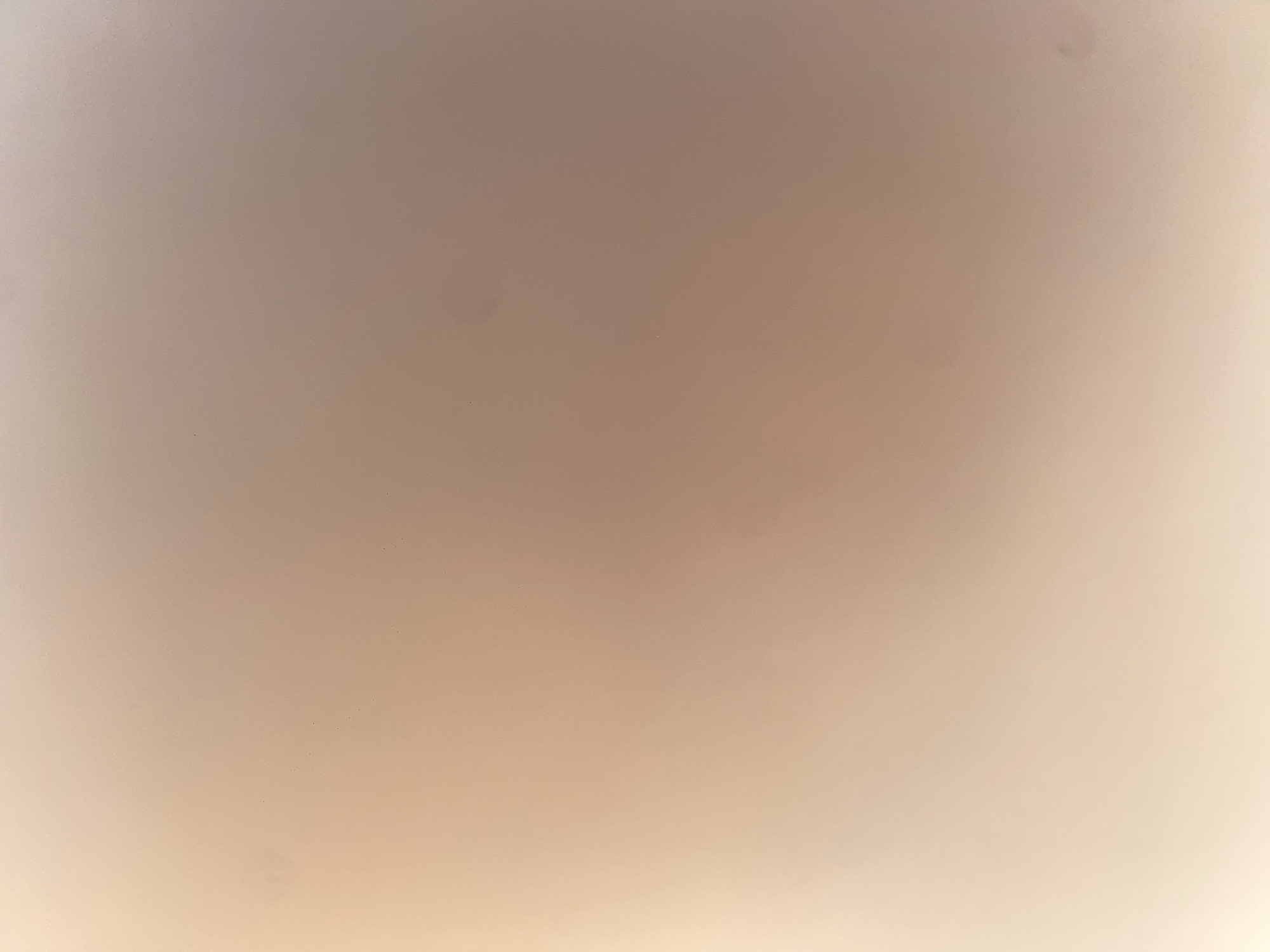 The image is a close-up, out-of-focus shot of a smooth, light-colored surface, possibly a wall or ceiling, with subtle variations in tone. There are a few small, dark specks visible, which appear to be dust or minor imperfections on the surface. The lighting creates a gradient effect, with the left side of the image being brighter and transitioning to a slightly darker, more muted tone towards the right. There is no discernible detail of Ablanitsa, Bulgaria, or any specific objects, people, or actions in this image.