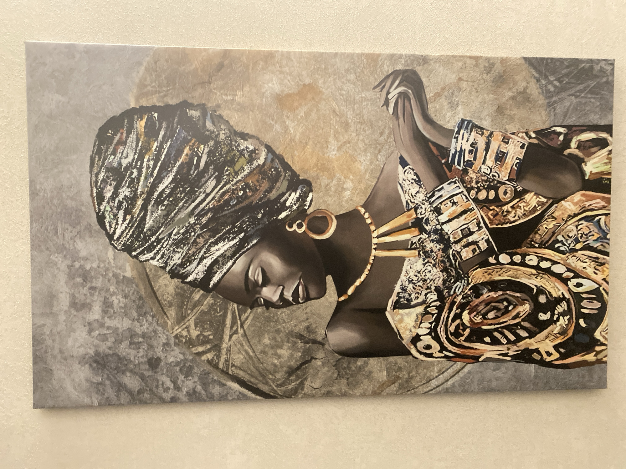 The image shows a canvas painting depicting a dark-skinned woman with a headwrap, gold jewelry, and patterned clothing. The background is a blend of gray and beige tones. The painting is hung on a light beige wall.
There is no information about the location in the city of Dzerzhinsk, Russia.