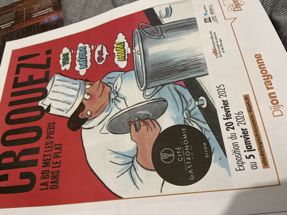 The image features a poster advertising an exhibition called "Croquez! La BD met les pieds dans le plat" at the Cité Internationale de la Gastronomie & du Vin in Dijon. The exhibition runs from February 20, 2025, to January 5, 2026. The poster depicts a chef character with thought bubbles labeled "Yumi," "Miam," "Yam...," and "Mmmm!" A website address, citedelagastronomie-dijon.fr, is also visible. Small icons of Angoulême, Dijon, and a text fragment, "la cito internationalo do la bando dossindo of do l'imago," appear in the upper right.