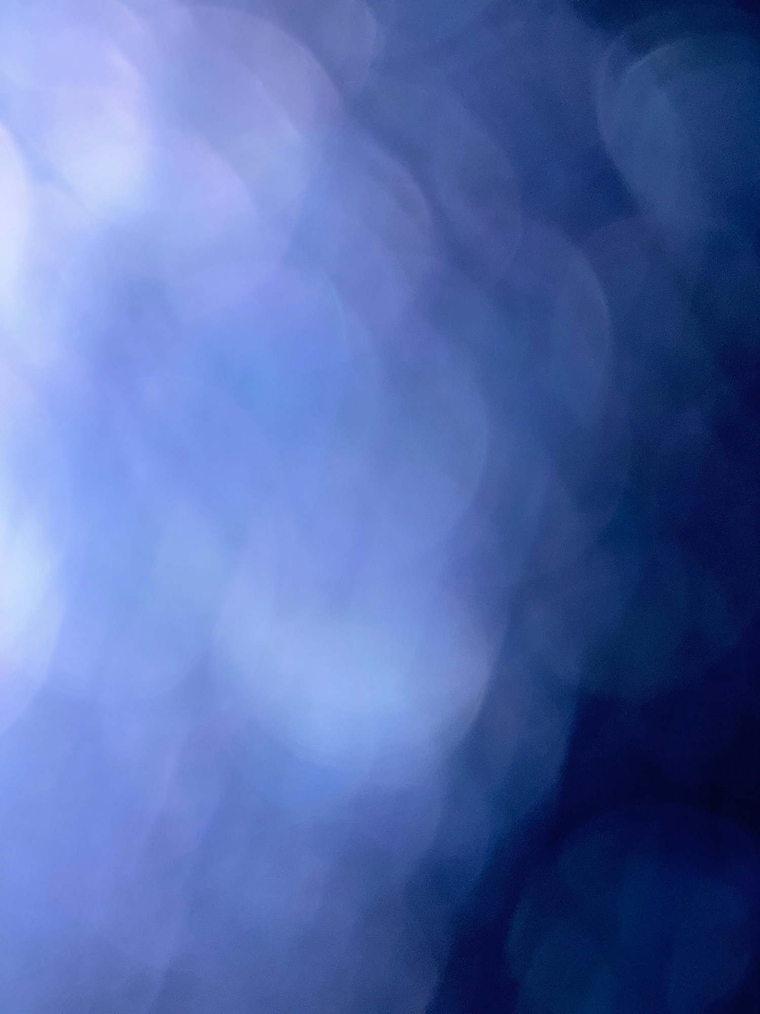 The image is an abstract, out-of-focus photograph with a bokeh effect. It features large, soft circles of light in varying shades of blue, ranging from a bright, almost white blue on the left to a deep, dark navy blue on the right. The lighting suggests a diffused, possibly artificial light source, creating a dreamy and ethereal atmosphere. There are no discernible landmarks, people, or specific objects within the frame, making it impossible to determine a location in Hong Kong or any other city. The image's abstract nature focuses solely on the interplay of light and color.