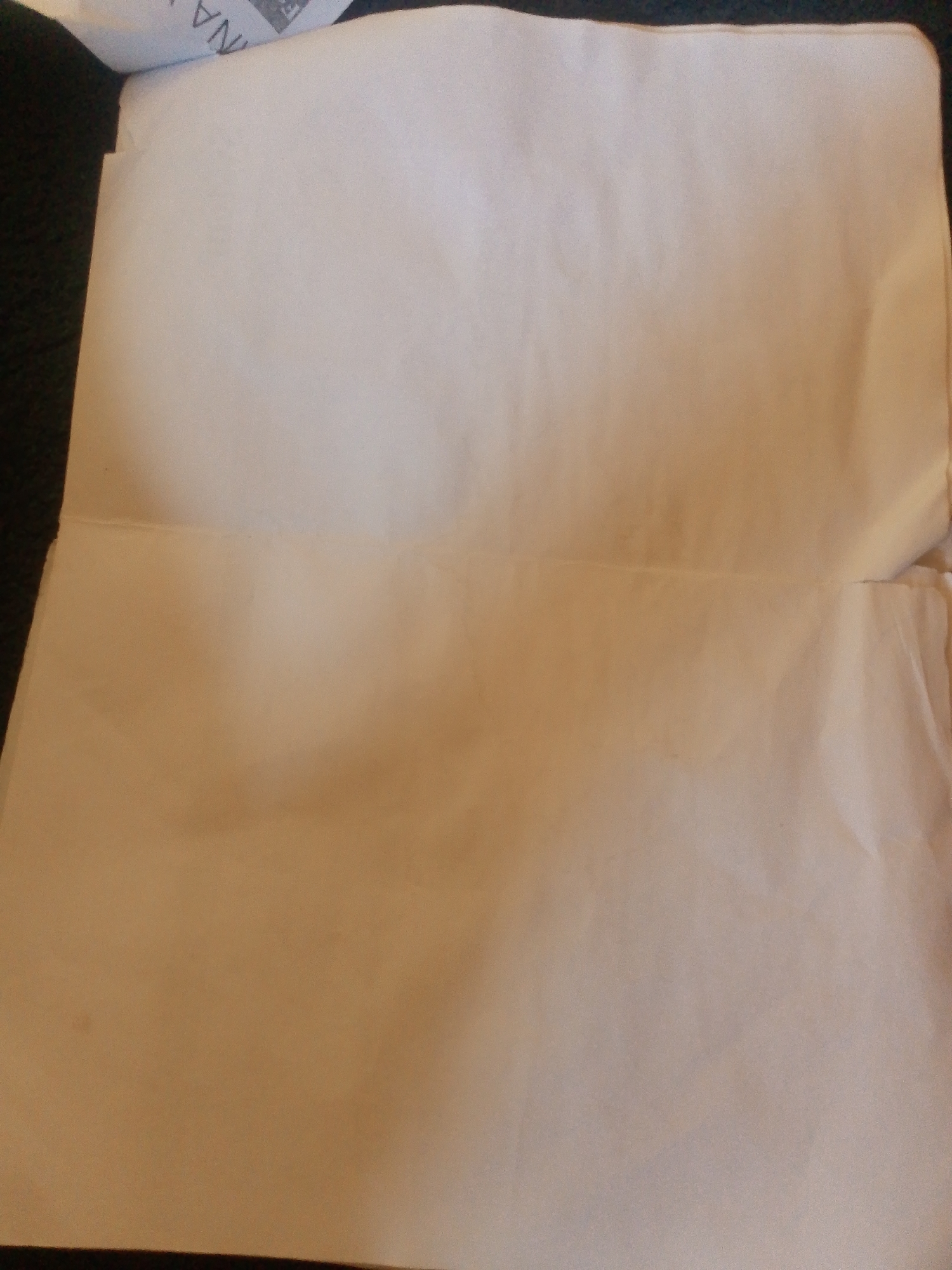 The image shows a close-up view of a folded piece of off-white paper, possibly a document or a letter. The paper appears to be creased horizontally across the middle. There is a hint of text, possibly "NA", visible in the upper left corner, suggesting it is part of a larger document. The background is dark and out of focus, hinting at a surface or object the paper is resting on. There are no people or specific objects that would allow for the determination of a location in Jalingo, Nigeria.