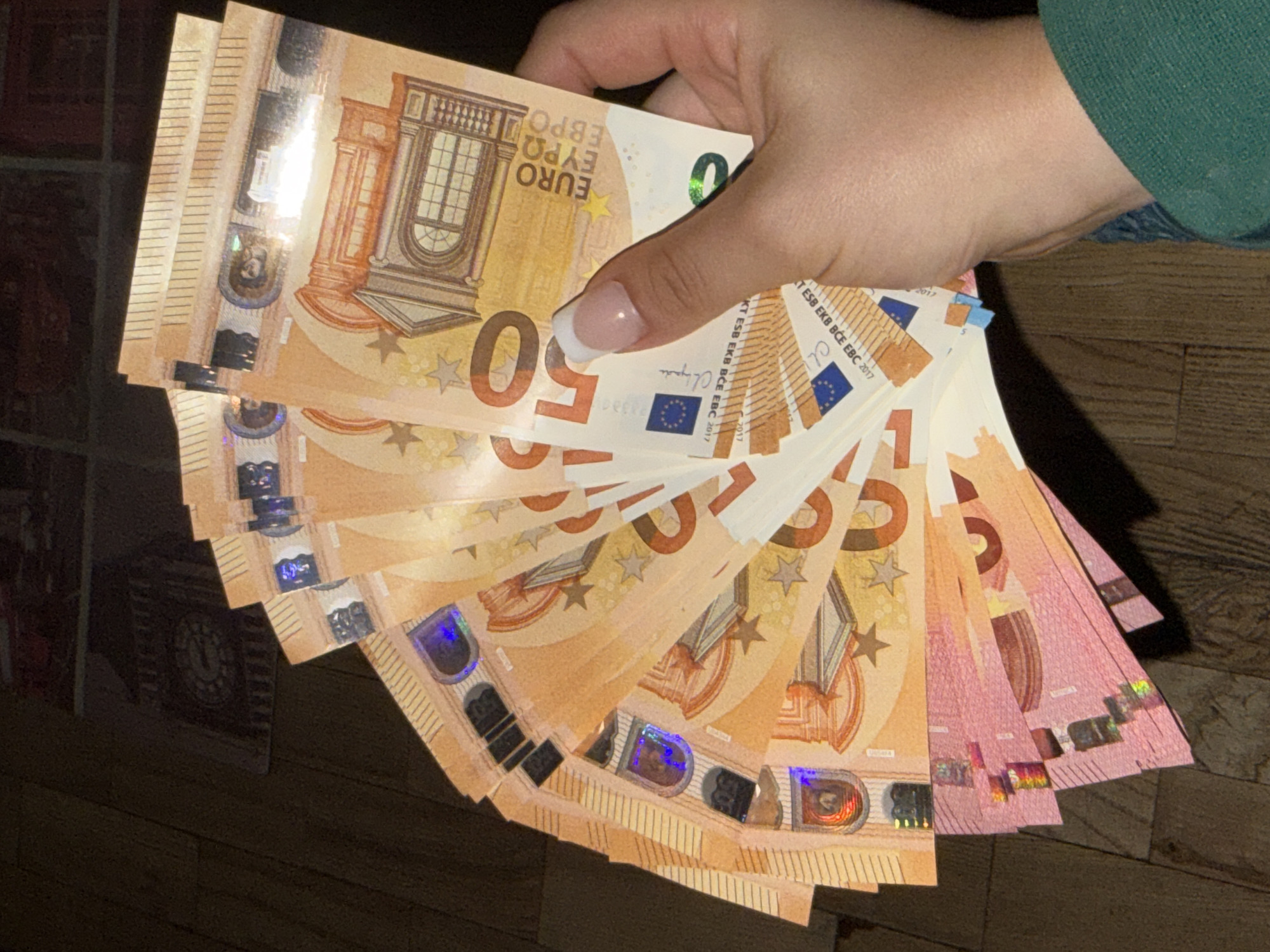 A hand holds a fan of euro banknotes. The majority of the notes appear to be 50 euro bills, but there are also some 10 euro bills. The background is dark. The image does not contain sufficient information to determine the location in Varna, Bulgaria.