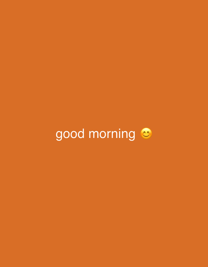 The media file displays a simple graphic with a solid, vibrant orange background. Centered horizontally on this background, white text spells out "good morning" in a sans-serif font. To the right of the text, a yellow smiling face emoji with closed eyes and rosy cheeks is present, conveying a cheerful and positive sentiment. The image suggests a morning greeting, but provides no specific visual cues regarding the time of day, weather, or location beyond the text and emoji themselves. There are no people or specific objects depicted other than the text and emoji. No visual details are present to indicate the location is Saint Petersburg, Russia.