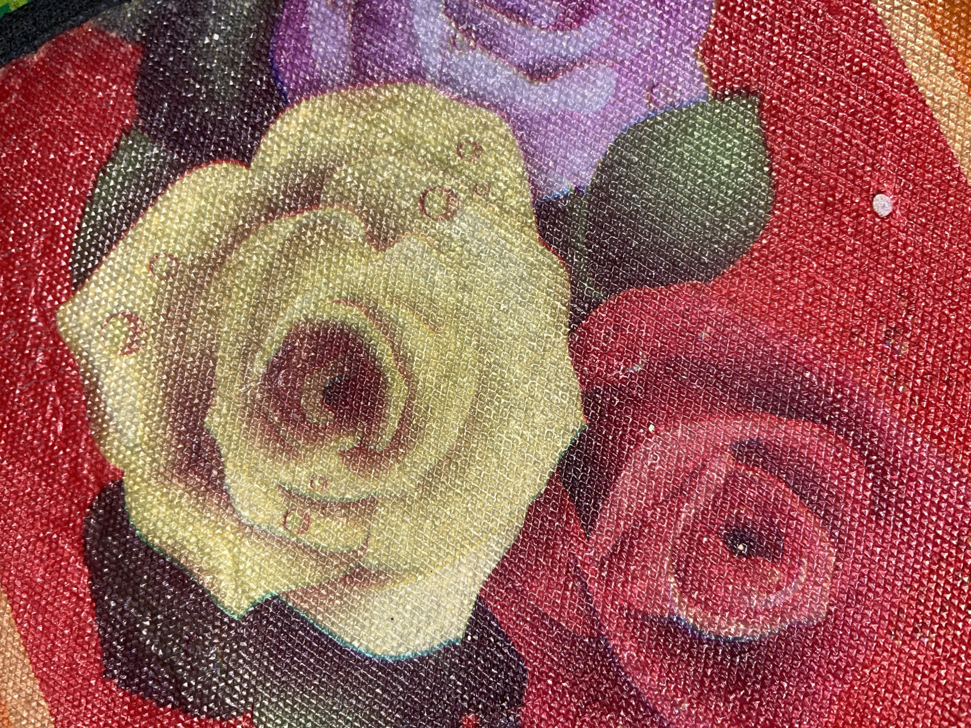 The image is a close-up, high-angle shot of a textured fabric with a floral print. The print features several roses in various colors, including yellow, red, and purple, with some dark areas that could be shadows or other floral elements. The fabric has a visible mesh-like texture, giving the print a slightly raised and dimensional appearance. There are small, dewdrop-like highlights on some of the petals. The overall impression is one of a colorful and ornate textile. There is no visible indication of location in the city of Benuaraja, Indonesia, as the image focuses solely on the fabric pattern.