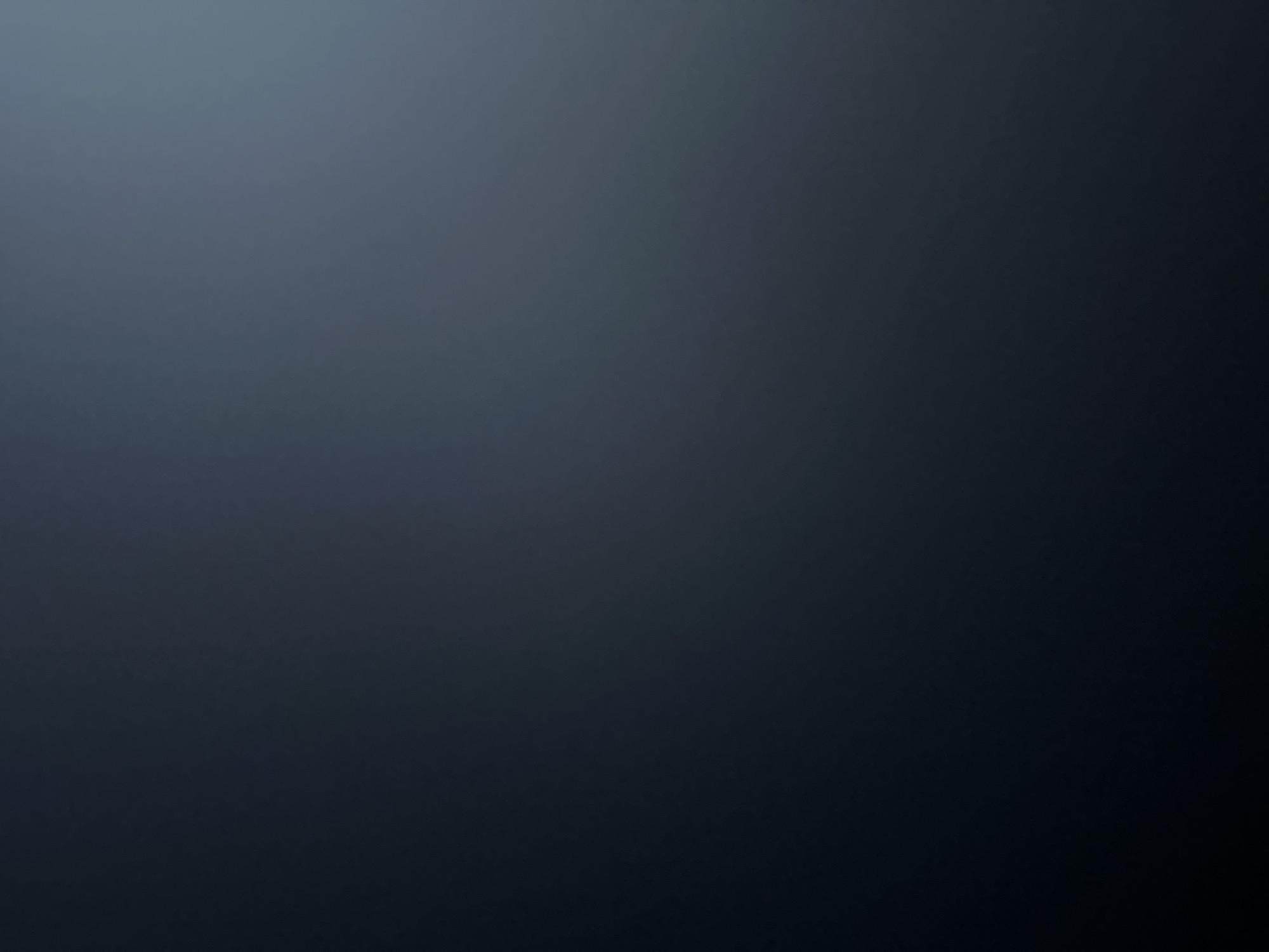 This is a dark, abstract background image. It is a gradient that transitions from a lighter, cool blue-grey at the top left to a very dark, almost black color at the bottom right. There are no discernible subjects, objects, or a specific scene. No activity or event is taking place. The image has a smooth, blurred texture, suggesting a digital or photographic effect rather than a natural environment. There are no visible text elements. The overall mood is dark and moody, with a subtle gradient that could be used as a backdrop. The lack of detail makes it impossible to determine a specific time of day, weather, or location cues.