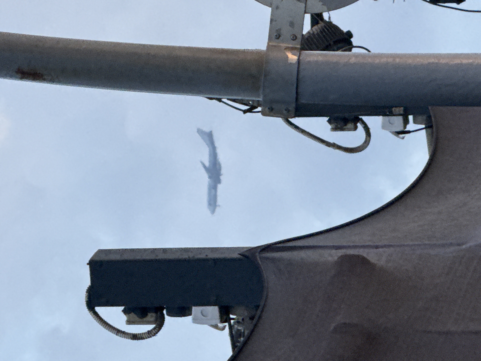 A medium shot shows an airplane silhouetted against a cloudy sky, framed by industrial infrastructure including a steel support beam, conduit and other mechanical hardware. The setting appears to be an urban environment. Specific location in Tel-Aviv, Israel cannot be determined based on the available visual data.