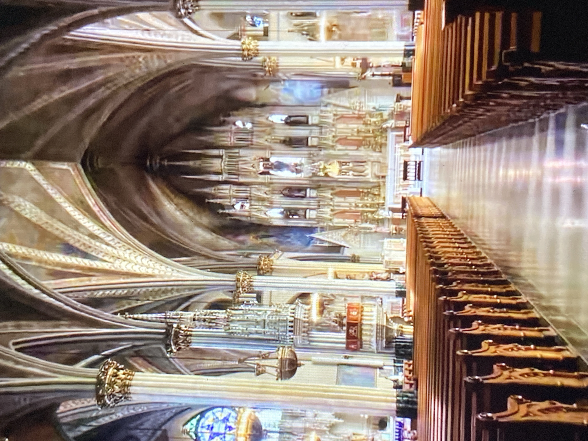 The image shows the interior of a grand, ornate cathedral. The architecture features vaulted ceilings, decorated columns, and detailed craftsmanship. Rows of wooden pews line the floor. Stained glass windows are visible. The building appears to be reflected in a polished floor surface. There is no indication of the city of Tinaquillo, Venezuela, or any people in the image.