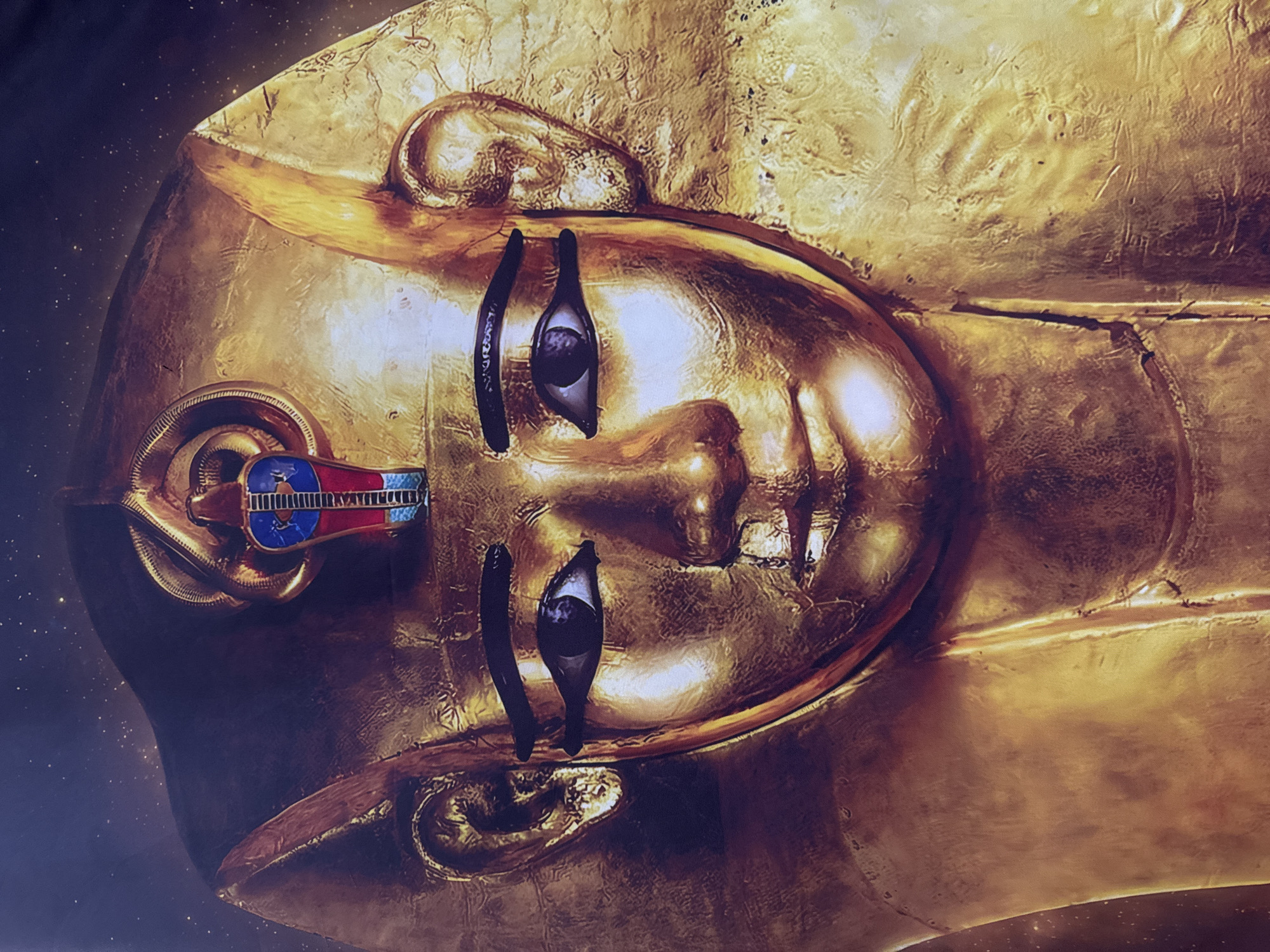 The image is a close-up, frontal view of a golden funerary mask. The mask depicts a stylized human face with dark, almond-shaped eyes outlined in black kohl. A golden headdress adorns the head, featuring a colorful striped pattern on the forehead and a coiled snake at the top. The mask is highly detailed, with subtle textures and contours that suggest a crafted, perhaps ancient, artifact. The background is dark and speckled with what appears to be faint starlight or glitter, creating a sense of depth and grandeur. The mask is not located in London, United Kingdom; it is a depiction of Tutankhamun's burial mask, which is housed in the Egyptian Museum in Cairo, Egypt.