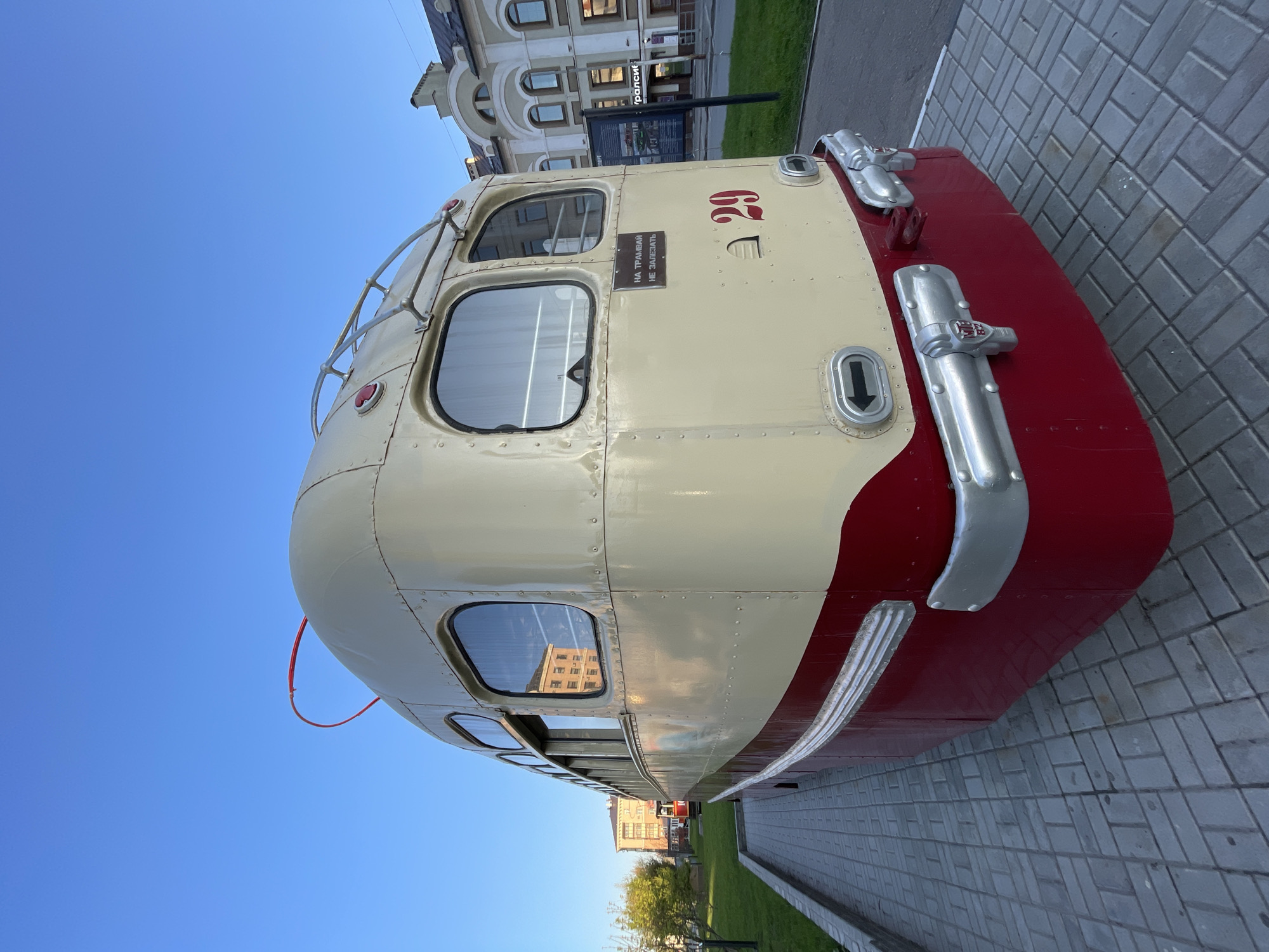 The image shows the front of a vintage, cream-colored tram with red accents, likely a historical display. It has two large windows reflecting nearby buildings. The tram is numbered "29" and bears a sign in Russian: "On Tramway, Don't Climb". The setting is an urban, paved area, possibly a pedestrian zone. The buildings and the sky suggest the city of Kazan, Russia.