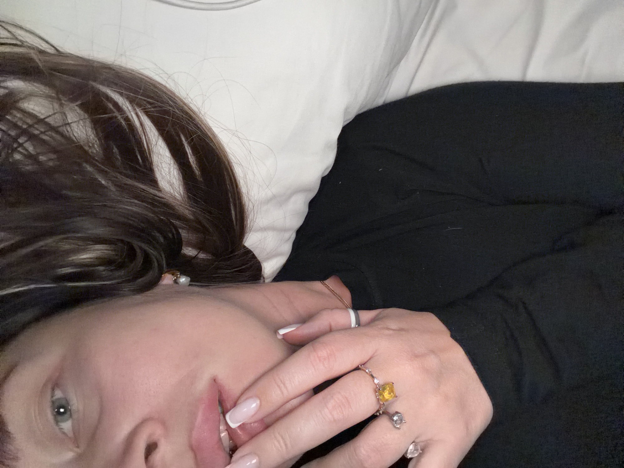 A woman with brown and blonde hair is lying on a white pillow wearing a black shirt. She is wearing several rings on her hand. The background is nondescript. There is no indication of the location being Moscow, Russia.