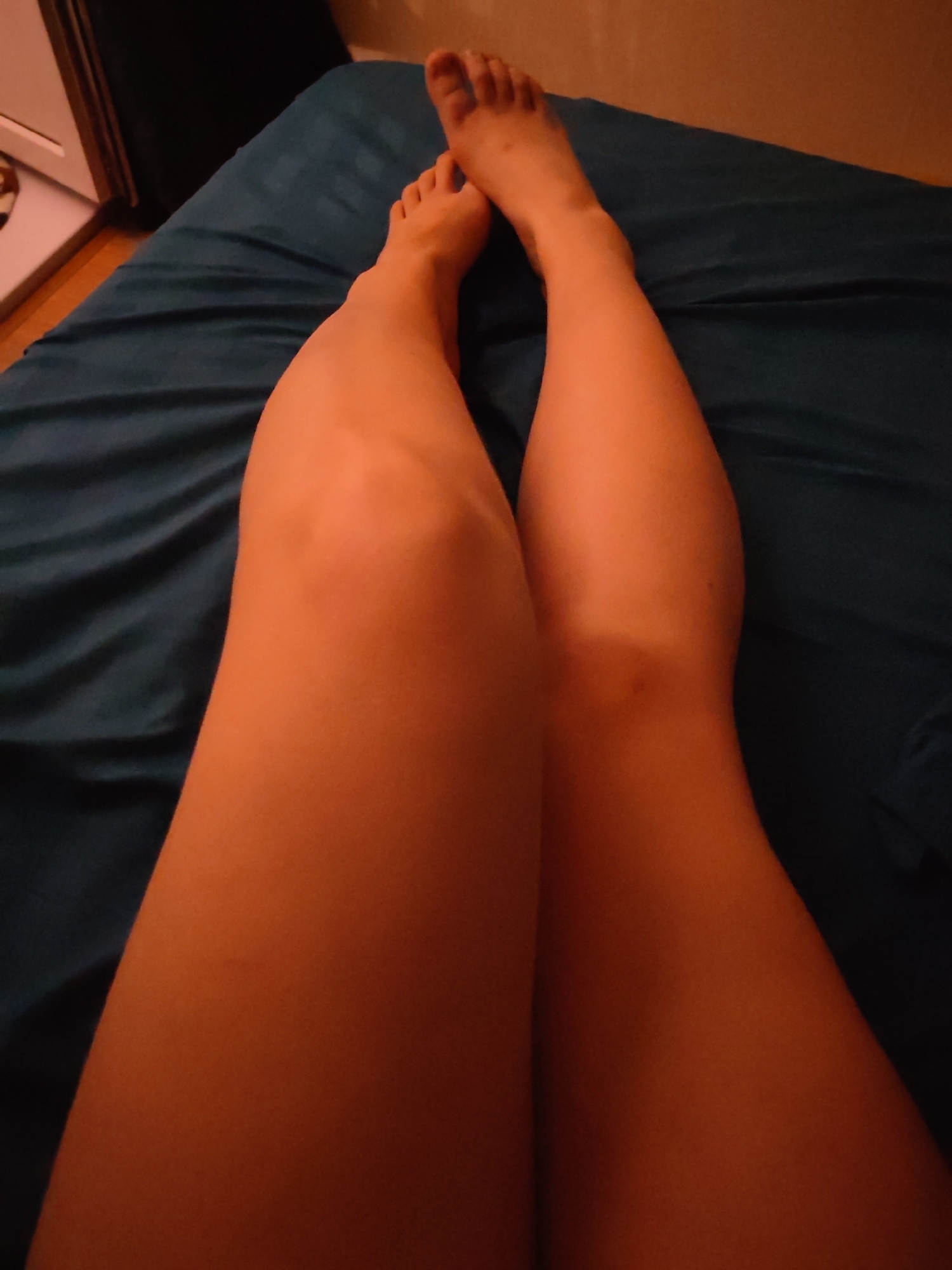 The image depicts a pair of legs lying on a blue bedsheet. The feet are visible at the top of the frame. No other people or objects are readily discernible. The location is not identifiable from the image.