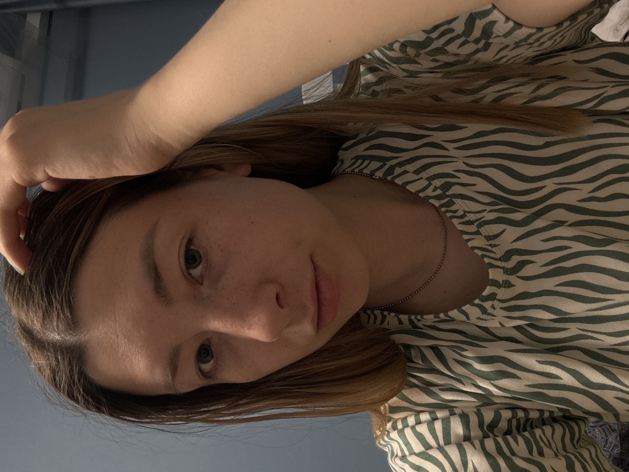 A young woman with light brown hair and fair skin is posing for a close-up photo. She is wearing a green and white zebra-striped top. Her left hand is resting on her head. She is wearing a silver chain necklace. The background is a solid, muted blue color. The image is angled, with the woman's face appearing in the lower center and her body extending to the upper right corner.
Moscow, Russia is not discernible from the image.