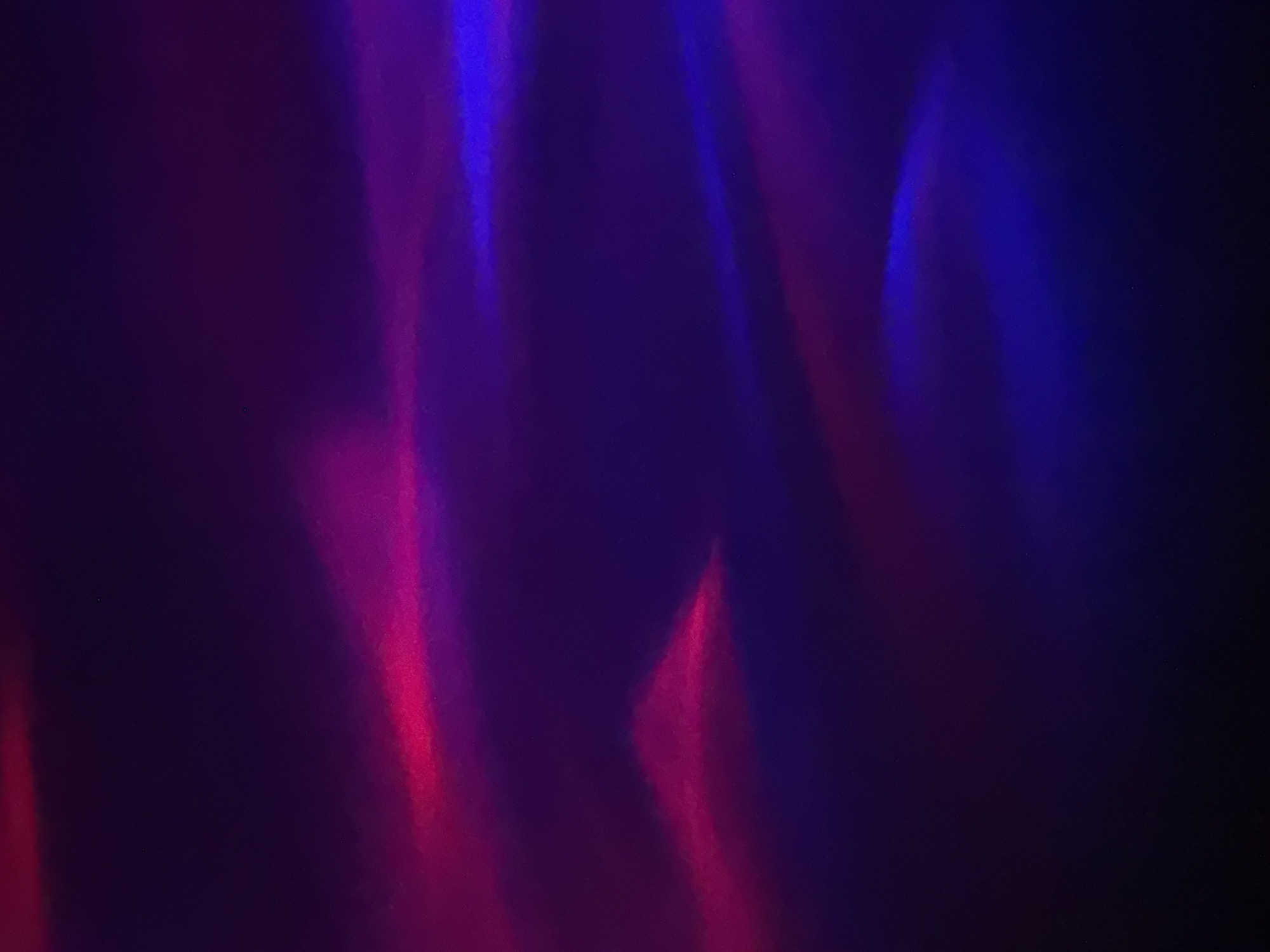 The image is a vertical, close-up, abstract photograph of light refractions and reflections on a dark, textured surface, possibly fabric or textured paper. The dominant colors are deep purple and shades of pink and blue, creating a gradient effect with streaks and wisps of lighter color against the dark background. The lighting appears to be dramatic, with bright, illuminated areas and deep shadows, suggesting a controlled lighting environment. There are no discernible people, objects, or discernible actions. The image does not contain any recognizable elements of Tiraspol, Moldova, or any urban environment.