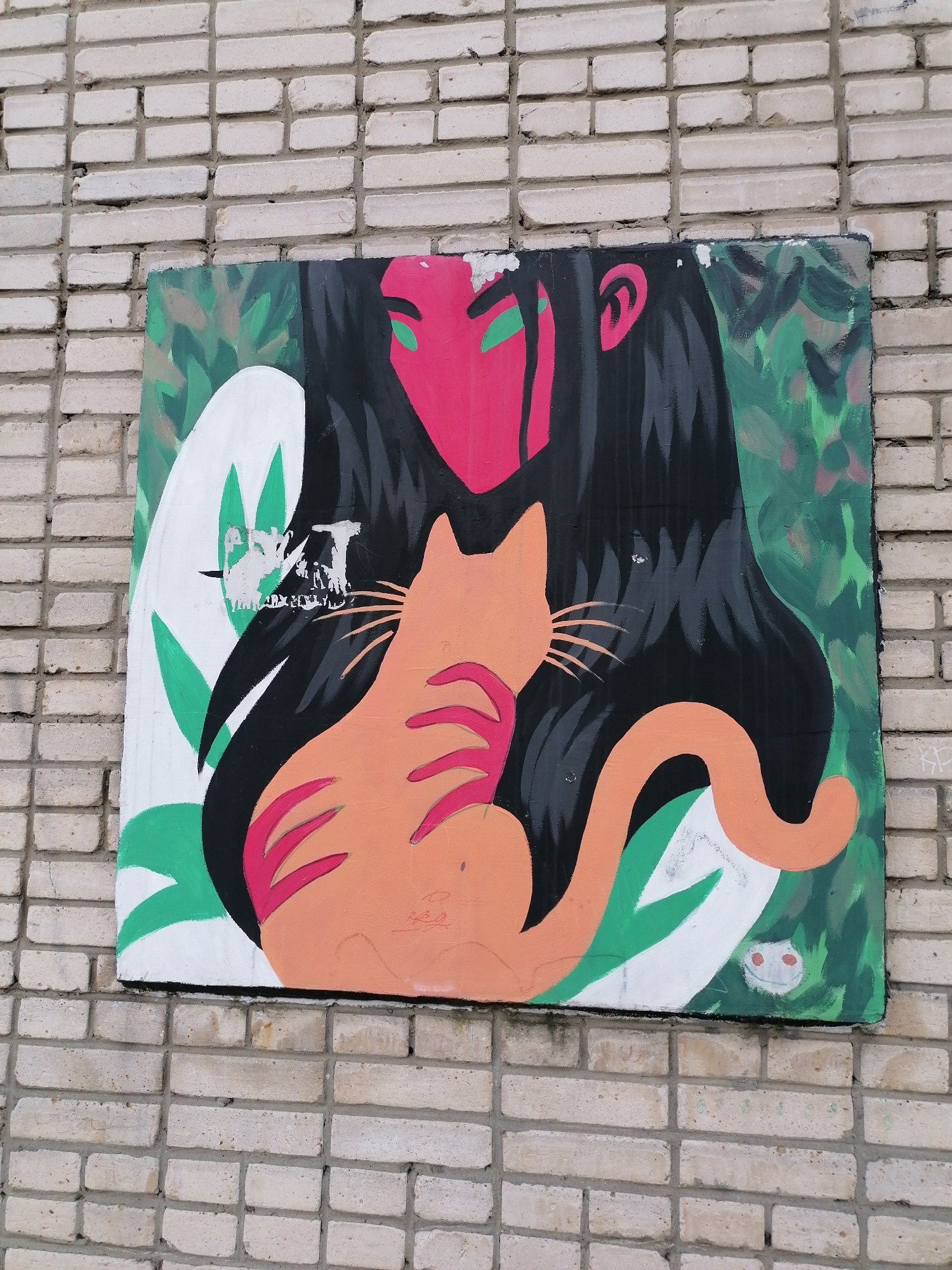 A rectangular artwork is affixed to a brick wall. The artwork depicts a red-faced figure with black hair and green eyes embracing an orange cat. The background consists of green and white foliage. There is some damage to the artwork, including what appears to be remnants of torn paper. The artwork is located in the city of Unknown, Unknown.