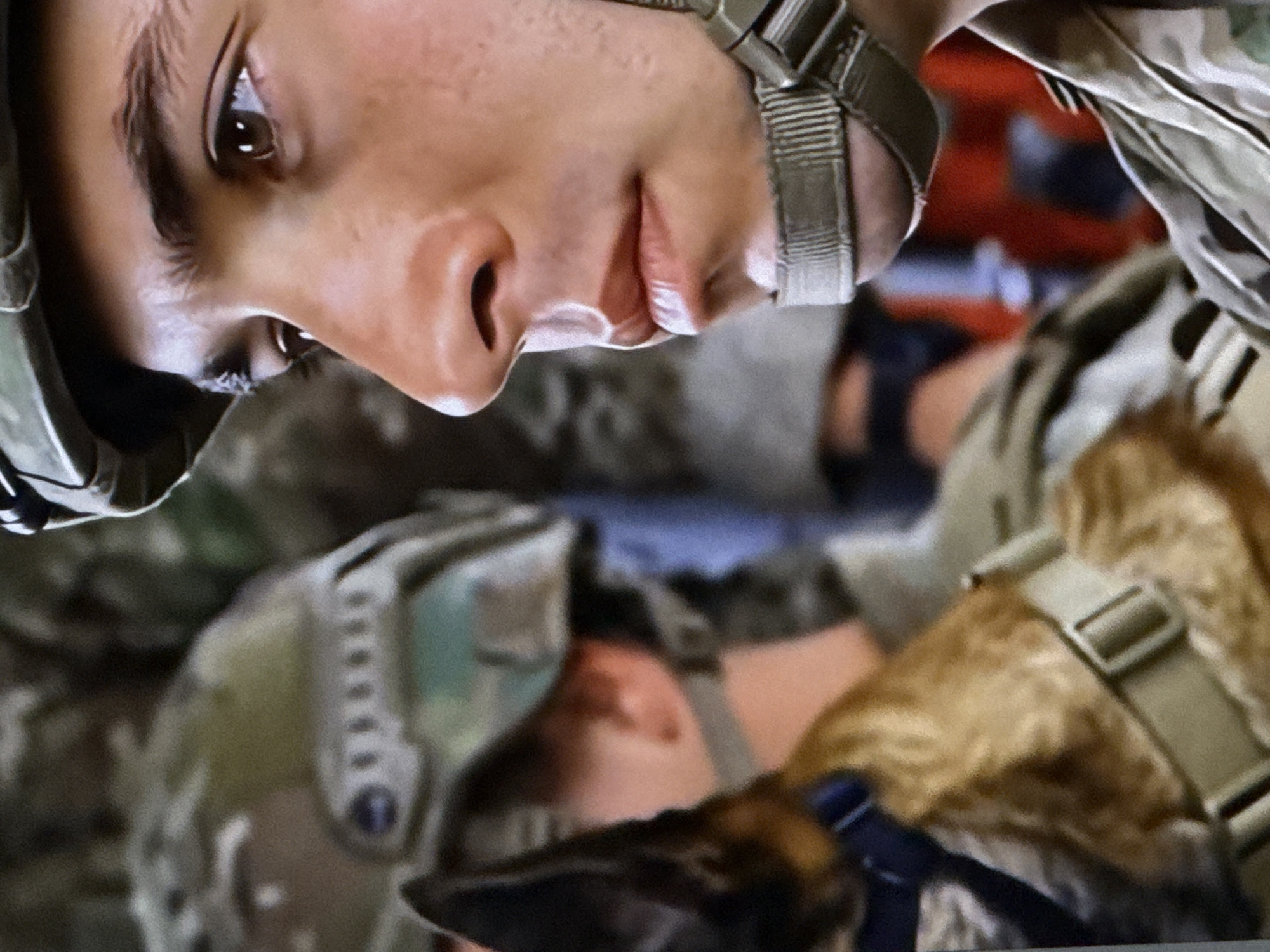 The image is a close-up, profile view of a young man wearing a military helmet and camouflage uniform. His face is turned to the right, with his right eye and part of his nose and mouth visible. The background is out of focus, showing other individuals in similar attire, suggesting a group setting. There are no recognizable landmarks or environmental cues to indicate the specific location within the city of Cahul, Moldova. The scene is static, with no apparent action or interaction occurring.