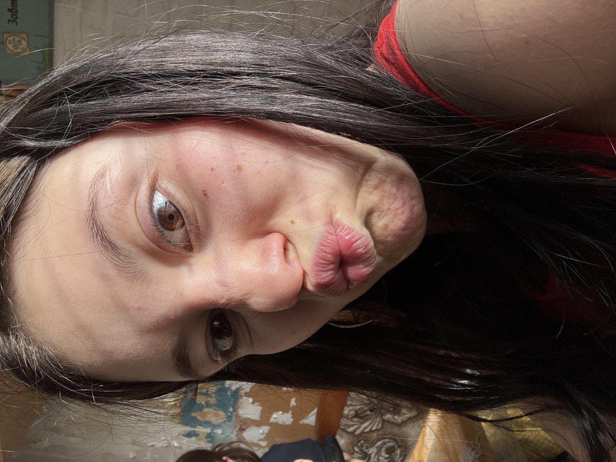 A medium shot depicts a young woman posing with pursed lips. She is viewed at an angle, with dark hair framing her face. The environment is nondescript. The information given does not specify that the photograph was taken in the city of Фоки, Russia, only that information was potentially available to describe this location.