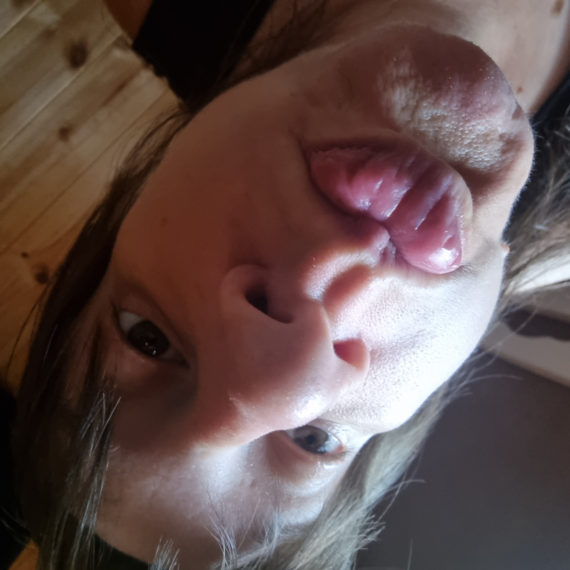 The image is a close-up, low-angle selfie of a person's face. The person is sticking their tongue out, and the lighting suggests an indoor environment with wooden paneling on the ceiling or wall in the background. The focus is primarily on the person's mouth and nose. There is no visible indication of the city of Dunnae-myeon, South Korea, or any other specific location.
