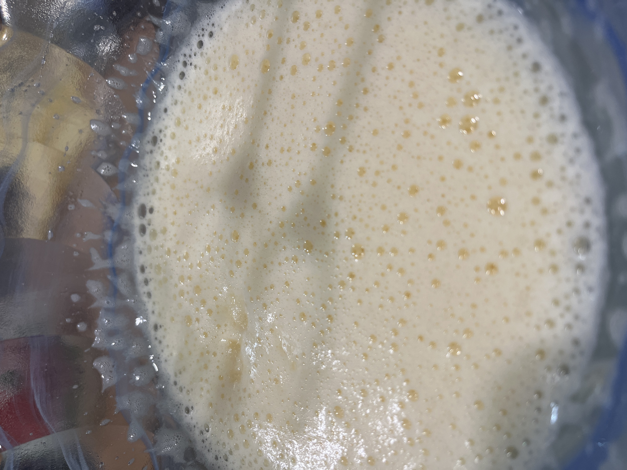 The image shows a close-up, overhead view of a yellowish-white, foamy liquid in a clear container. The container appears to be made of glass or plastic, and some residue is visible on the sides. The liquid is filled with small bubbles. The location is not apparent from the image.