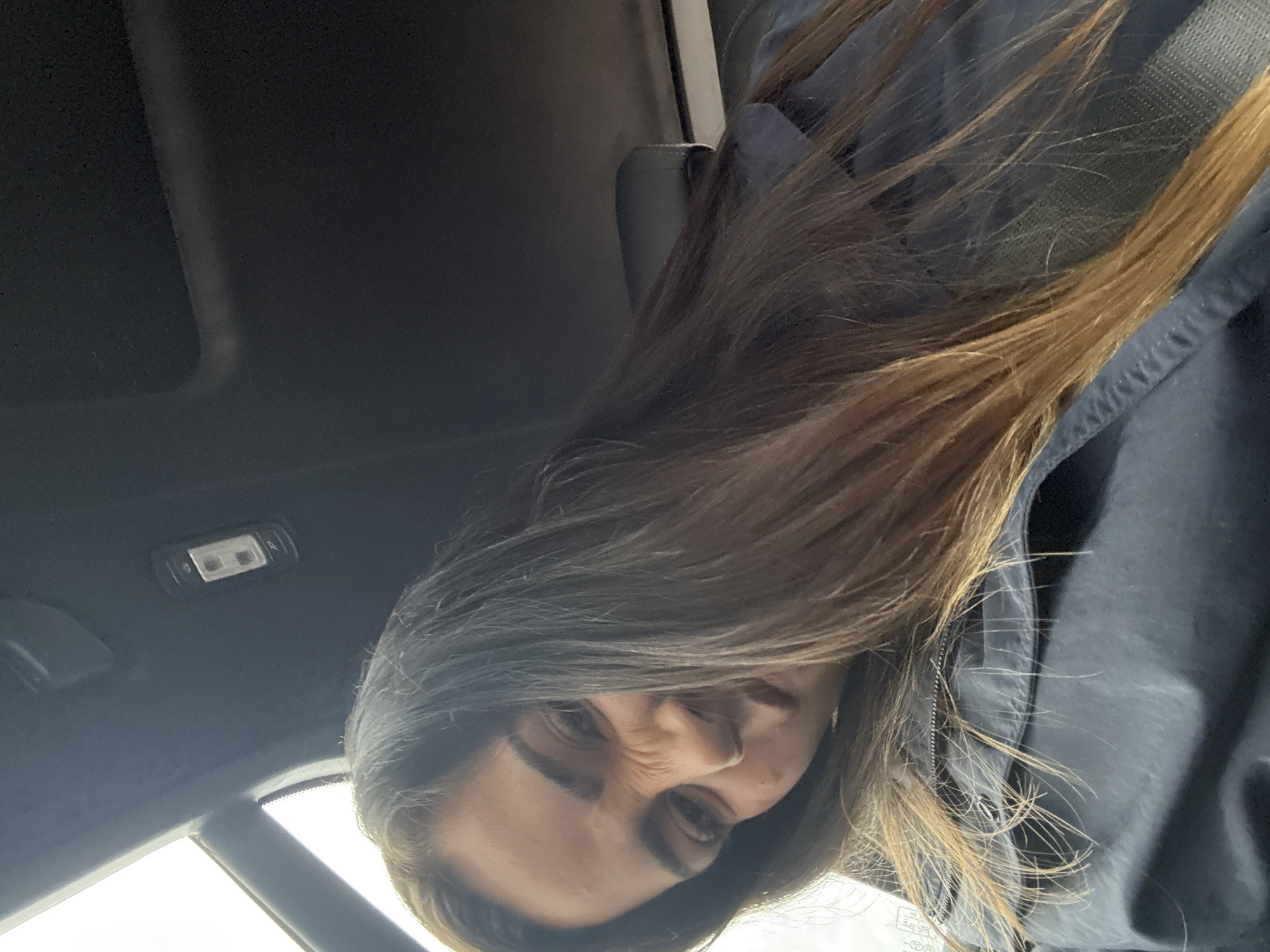 A person with long brown hair, wearing a dark jacket with the hood up, is upside down in what appears to be the interior of a car. The car's ceiling is visible in the upper left corner, with a light fixture. The scene is underexposed and slightly blurry. No information confirms a location in Santa Rita Tlahuapan, Mexico.