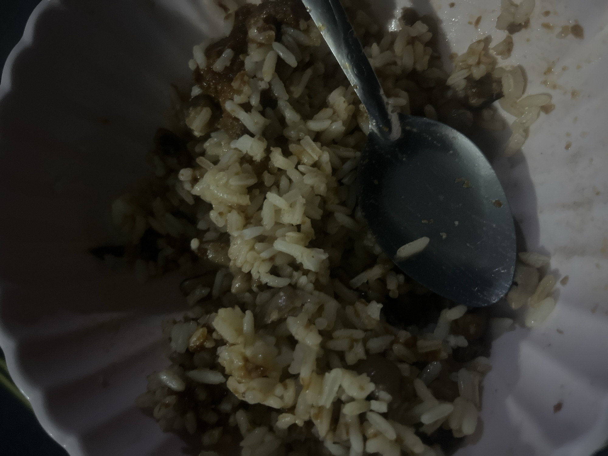 An overhead shot shows a pink bowl filled with rice and what appears to be small pieces of meat. A metal spoon is partially submerged in the food. The exact location within Gura Top, Nigeria cannot be determined from the image. No people are visible. The scene is indoors, likely a domestic setting.