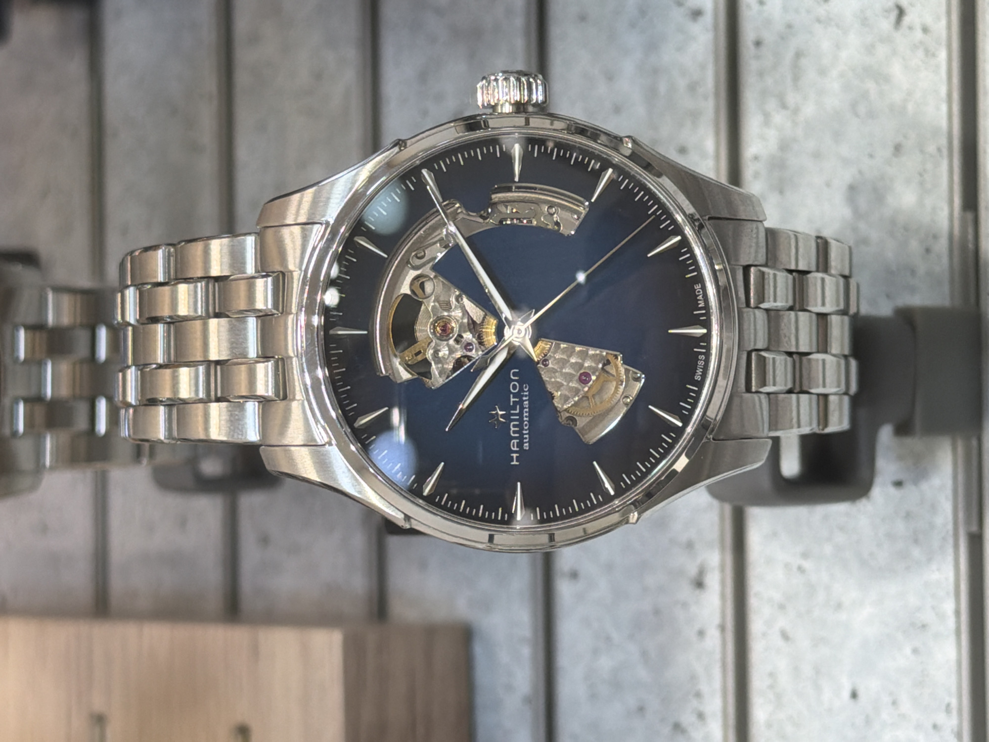 The image shows a Hamilton Automatic watch with a blue face and a partially open display of its inner workings. The watch has a silver-colored metal band. The watch is being displayed in a store; the background is blurred but appears to be a retail display. There is no information about a location in Yerevan, Armenia, in the image.