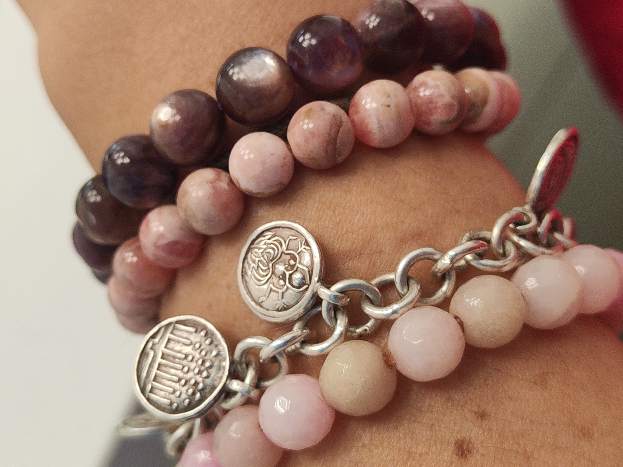 The image shows a person's arm adorned with three bracelets. The bracelets consist of round beads in varying shades of pink and purple. One bracelet appears to have silver charms connected by a silver chain. The background is blurred, making it difficult to determine the exact location. Based on the objects in the image, there is no indication or evidence to suggest this image was taken in Saint Petersburg, Russia.
