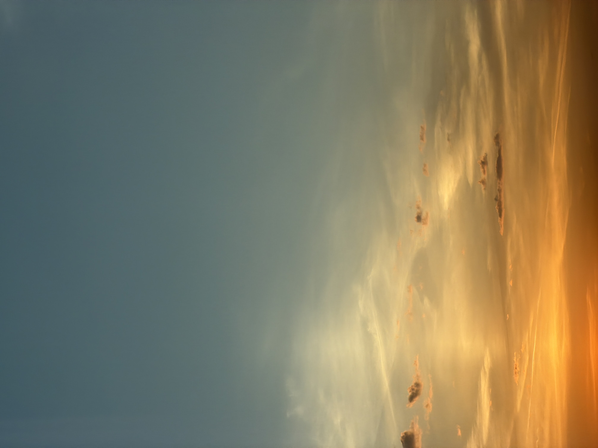 The image depicts a sunset sky. The left side of the image shows a clear, blue sky, transitioning to a golden and orange hue on the right side, where clouds are visible. The photograph appears to be taken outdoors. There is no visible indication of the location being in Khimki, Russia or any other city. No people, objects, or interactions are depicted other than the clouds in the sky.