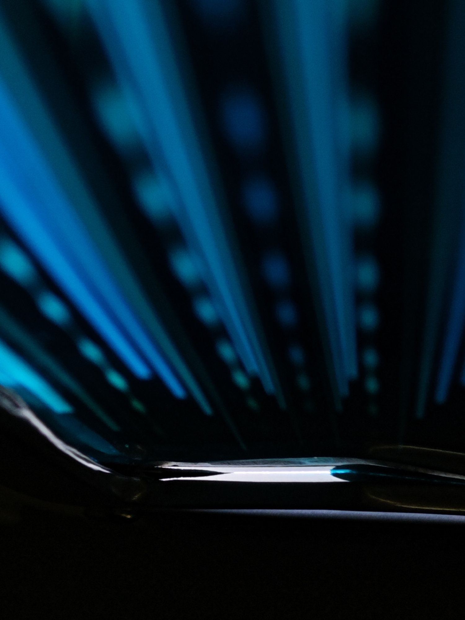 The image is an abstract, low-angle shot of blue light streaks emanating from a dark foreground. The streaks are sharp and dynamic, creating a sense of speed and movement. The foreground appears to be a glossy, dark surface, possibly a table or floor, with a bright reflection of the light streaks. The background is dark and out of focus, with some blurred circular shapes that could be lights or bokeh effects.
There are no people or identifiable objects visible in the image. The scene is devoid of any context that would place it in Bờ Y, Vietnam. The abstract nature of the image makes it impossible to determine the exact location or any specific details about the environment.