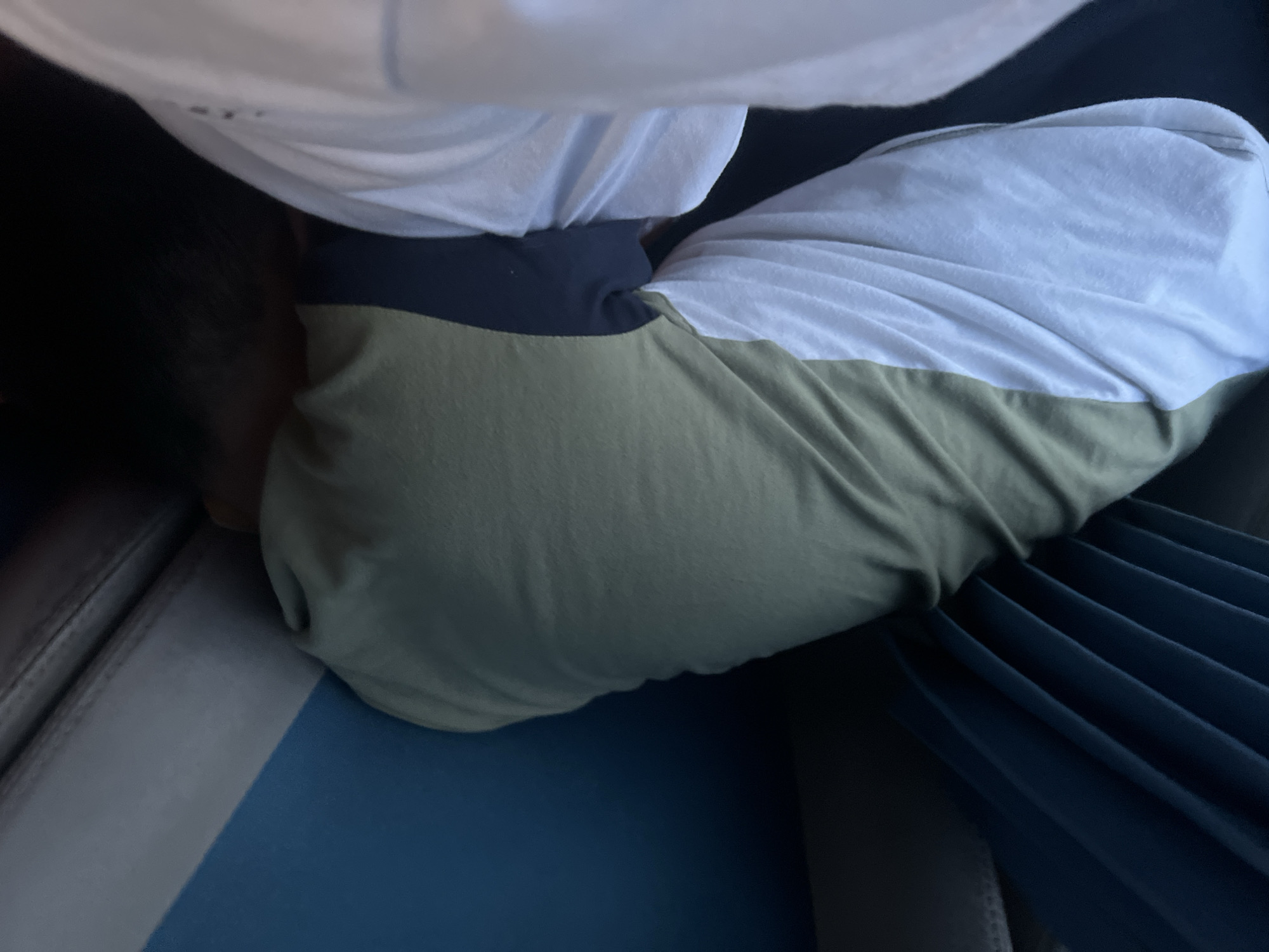 The image shows a close-up view of a person from the waist down, lying on their side. The subject is wearing a white t-shirt with a dark blue band across the top of the waistline and olive green pants. The person appears to be resting or sleeping, with their head not visible in the frame.
The person is positioned on a surface that looks like a seat, possibly in a vehicle or waiting area, with a dark blue pleated fabric visible to the right. The seat has a textured gray and blue upholstery. The lighting suggests it could be daytime, but there are no clear indicators of the time of day or weather. The overall scene is intimate and appears to capture a moment of repose.
There is no visible text in the image. The context provided places the location in Davao City, Philippines.