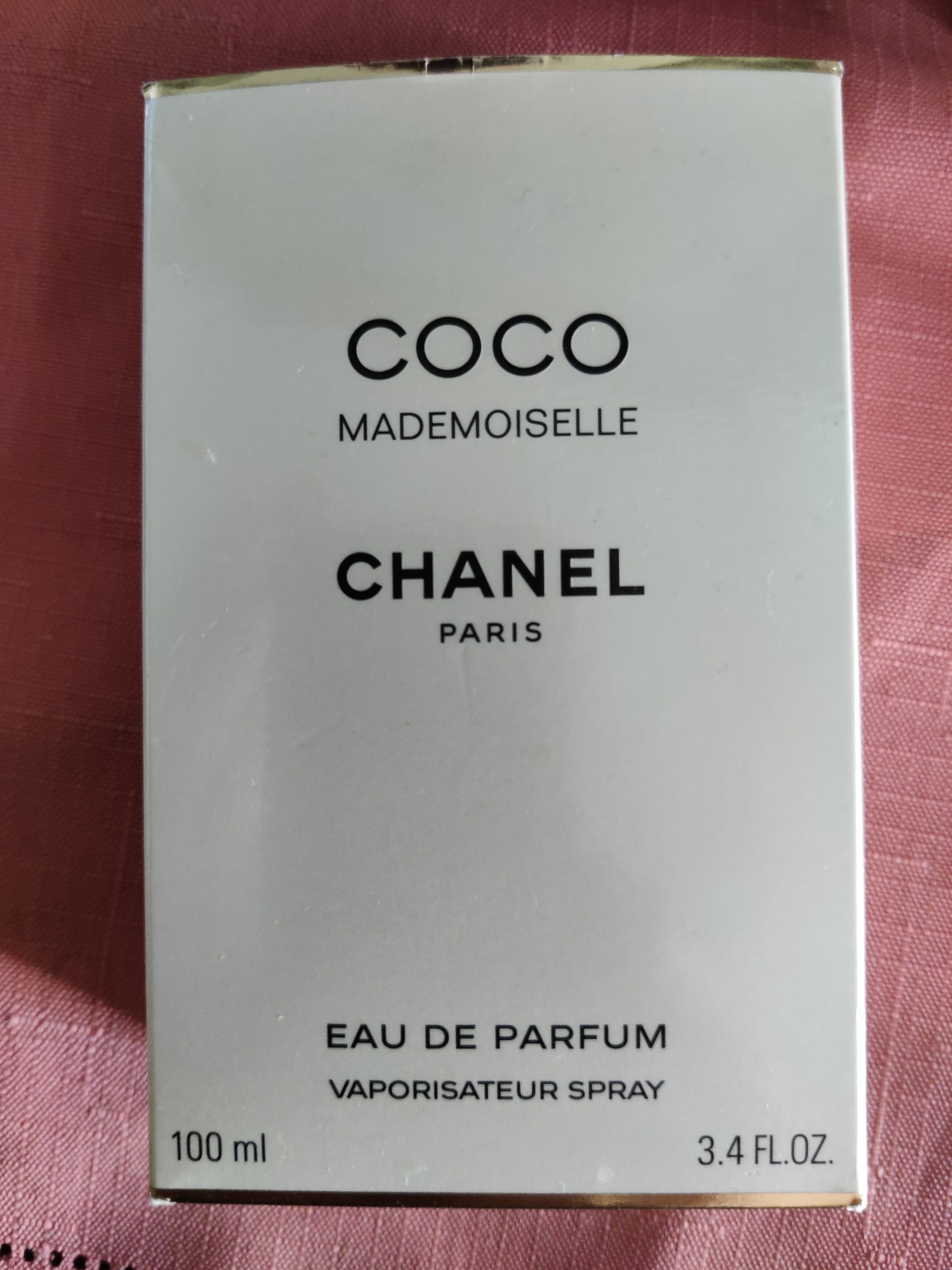 A white box for Chanel COCO MADEMOISELLE EAU DE PARFUM is displayed on a pink, textured surface. The box has black lettering that reads "COCO MADEMOISELLE" at the top, followed by "CHANEL PARIS" in a larger font. Below that, "EAU DE PARFUM" and "VAPORISATEUR SPRAY" are written. The left side of the box shows "100 ml", and the right side shows "3.4 FL.OZ.". The image does not provide information about the location in the city of Lower Paxton Township, United States of America.