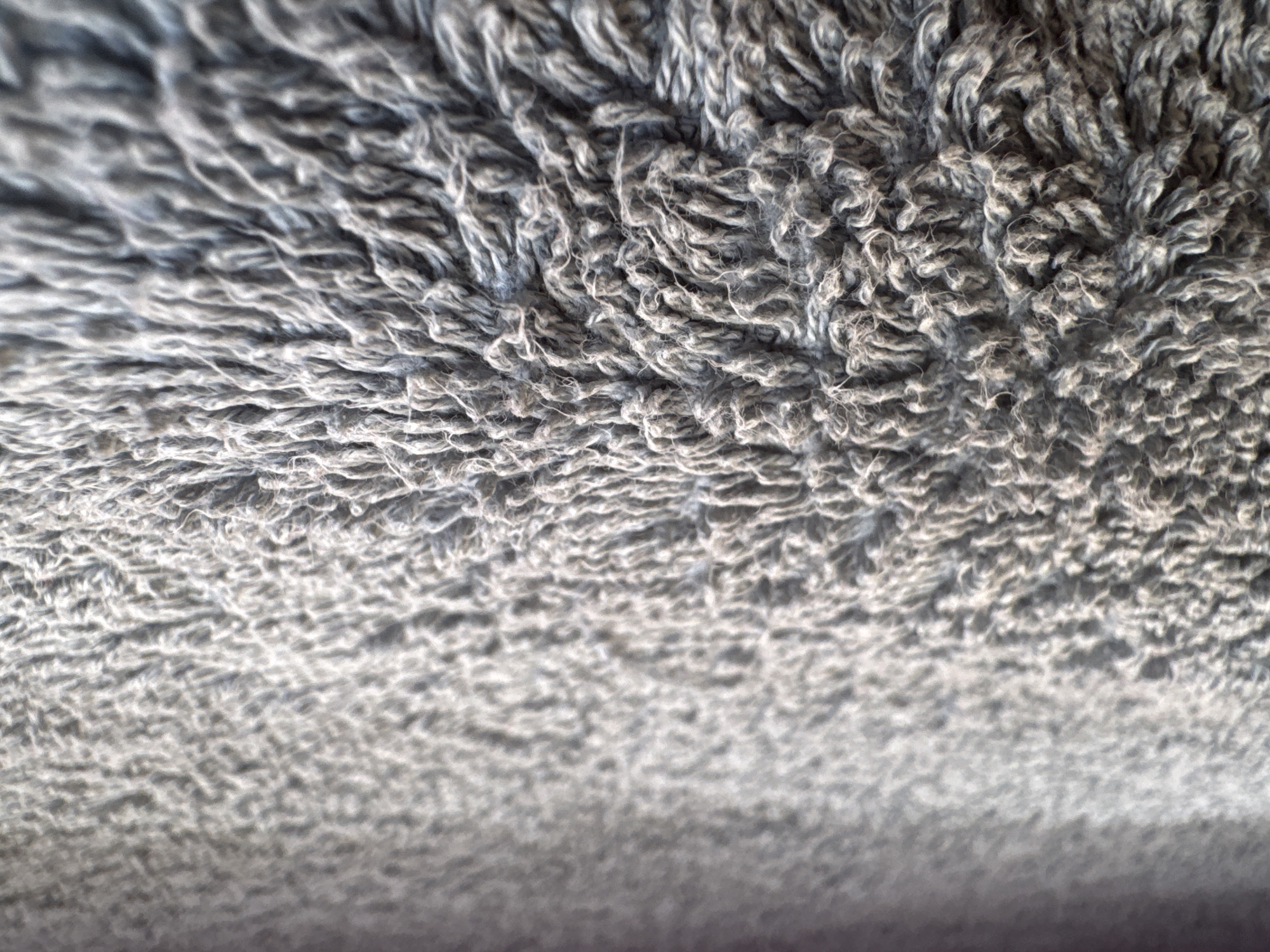 The image shows a close-up of a gray, textured surface, likely a rug or fabric. The texture consists of intertwined fibers or threads, creating a dense, pile-like appearance. The foreground is in focus, showcasing the individual strands, while the background gradually blurs, giving a sense of depth. No people, objects, or actions are visible. The location is Unknown, Unknown.