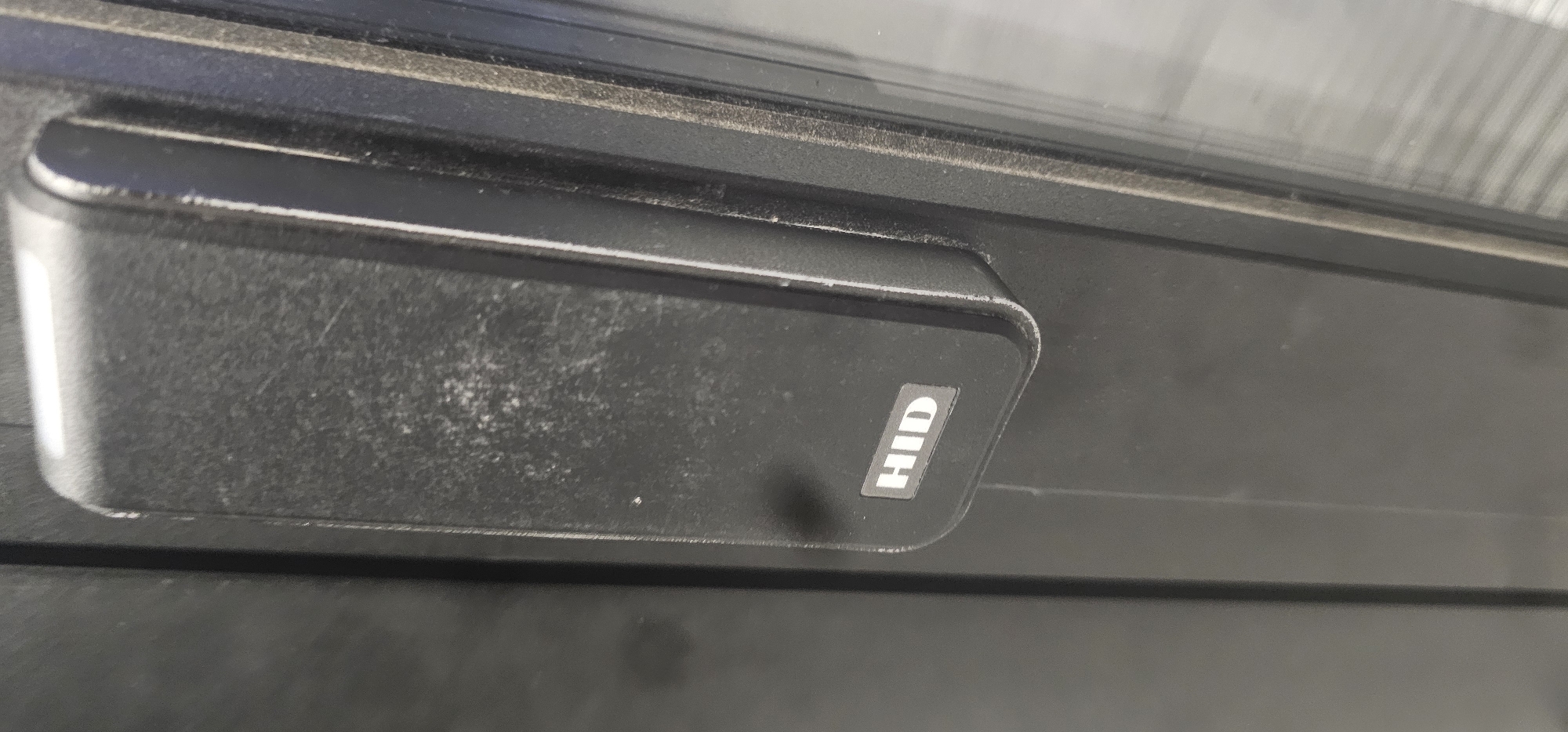 A close-up shot shows a black HID card reader mounted on a dark, possibly black metal surface. The reader has a rectangular shape with rounded edges and a slight curvature. The "HID" logo is prominently displayed on a sticker attached to the right side of the reader. The surface around the reader and the reader itself appears slightly dusty or dirty. Based on the prevalence of HID card readers in various access control systems, and without additional contextual information, it's impossible to confirm a specific location in Sofia, Bulgaria. Additional contextual elements would be needed to ascertain the specific location.