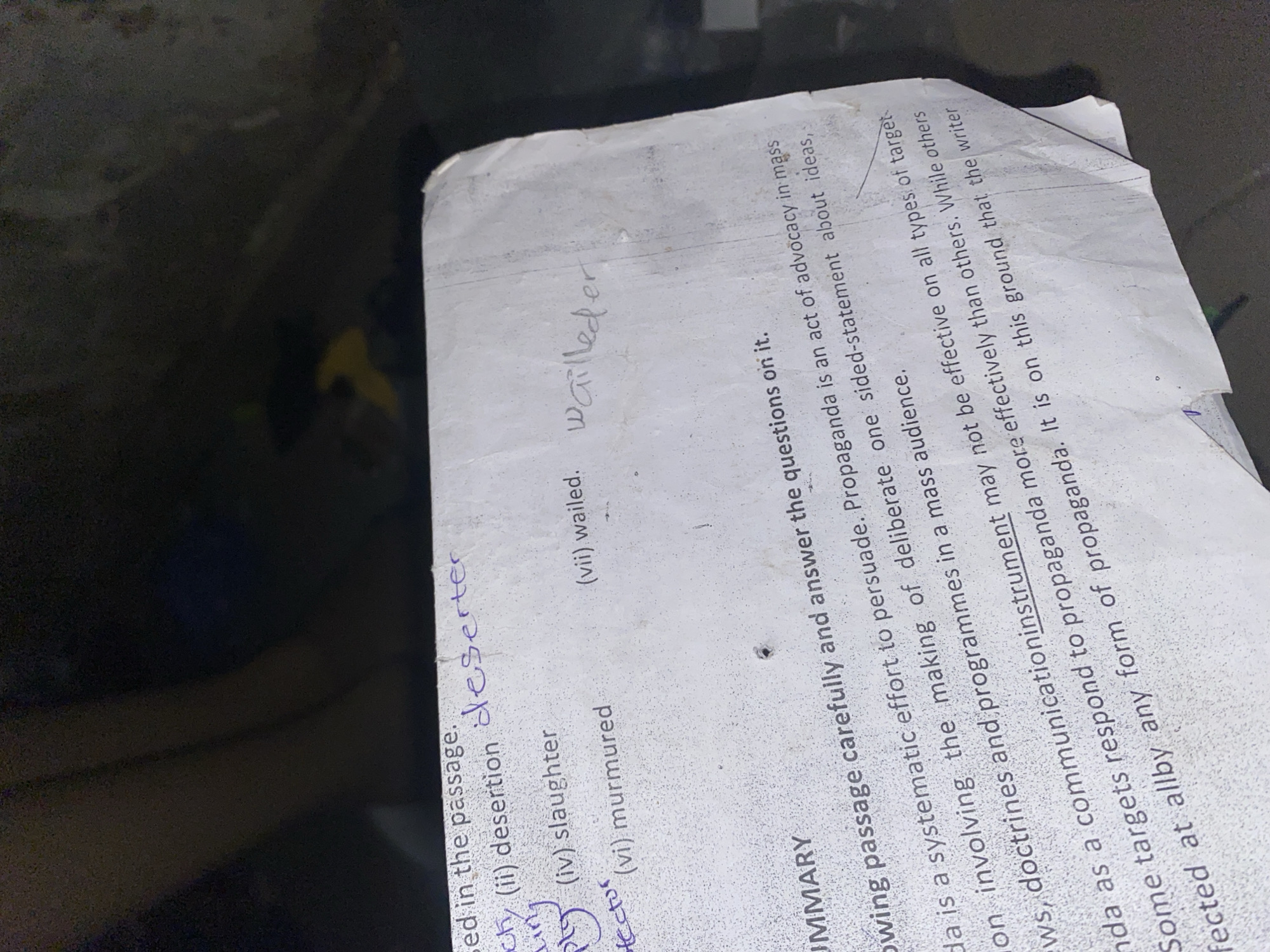 The image displays a close-up view of a crumpled piece of paper with handwritten text and printed text, lying on a dark, textured surface that suggests an outdoor or dimly lit environment, possibly on the ground. The paper itself has several items listed with Roman numerals, some of which are circled in purple ink, and some circled words are crossed out. For example, "(ii) desertion" is present and has "deserter" written next to it in purple. "(iv) slaughter" and "(vi) murmured" are also visible. Another section of the paper contains printed text, seemingly an excerpt about propaganda, with the word "instrument" underlined. Handwritten text "wailled er" is written in pencil in the upper right portion of the paper. The lighting in the image is poor, casting shadows and making some details difficult to discern. The overall impression is that of discarded or used paper found in a natural or unkempt setting. The prompt's request to include "the location in the city of Jauro Yinu, Nigeria" is impossible to fulfill as there are no visual cues in the image to support this specific location.
