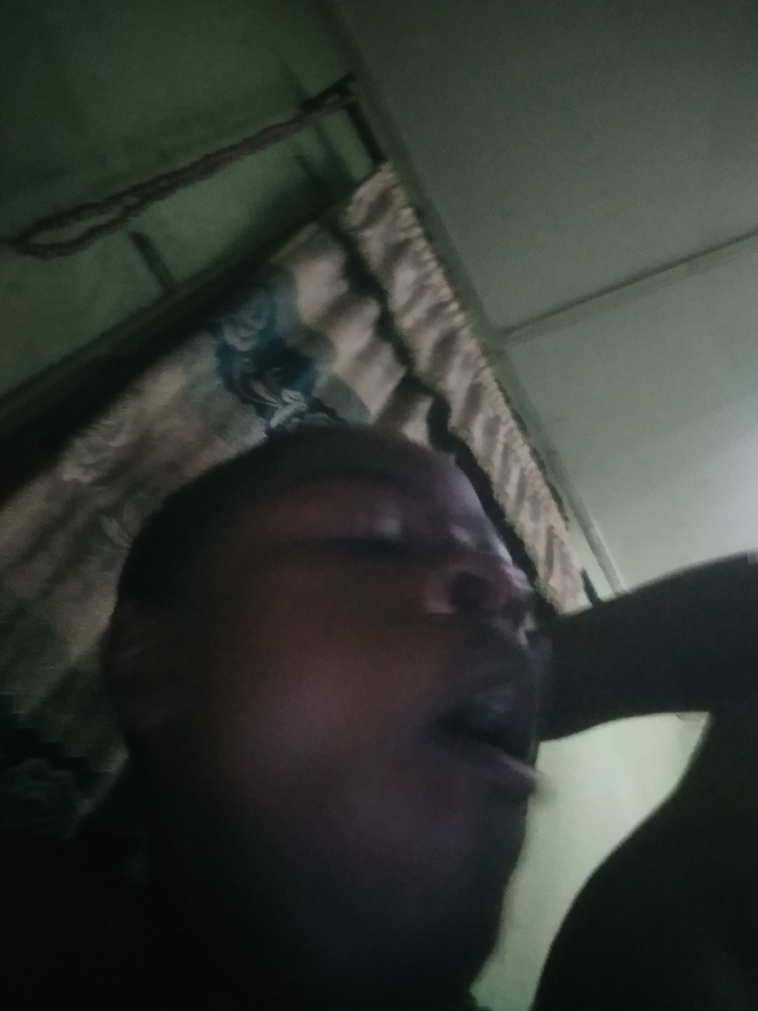 A close-up, dimly lit image shows a person lying down, with their mouth slightly open. A curtain hangs above them. The location is possibly a bedroom, based on the presence of the curtain. The location is Shangisha, Nigeria, based on the prompt.