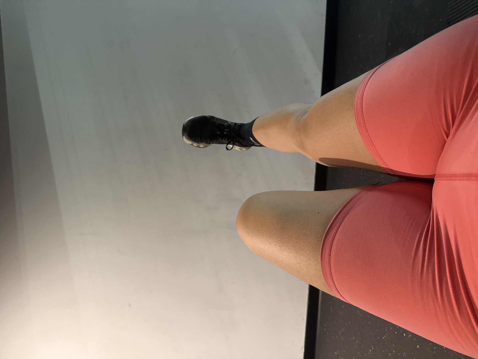 The image shows a low-angle shot of a person's legs, wearing pink shorts and black athletic shoes. The person's right leg is extended upwards and to the left, while the left leg is bent at the knee. The background is a plain, light-colored wall. There is no indication of the location being Paris, France.
