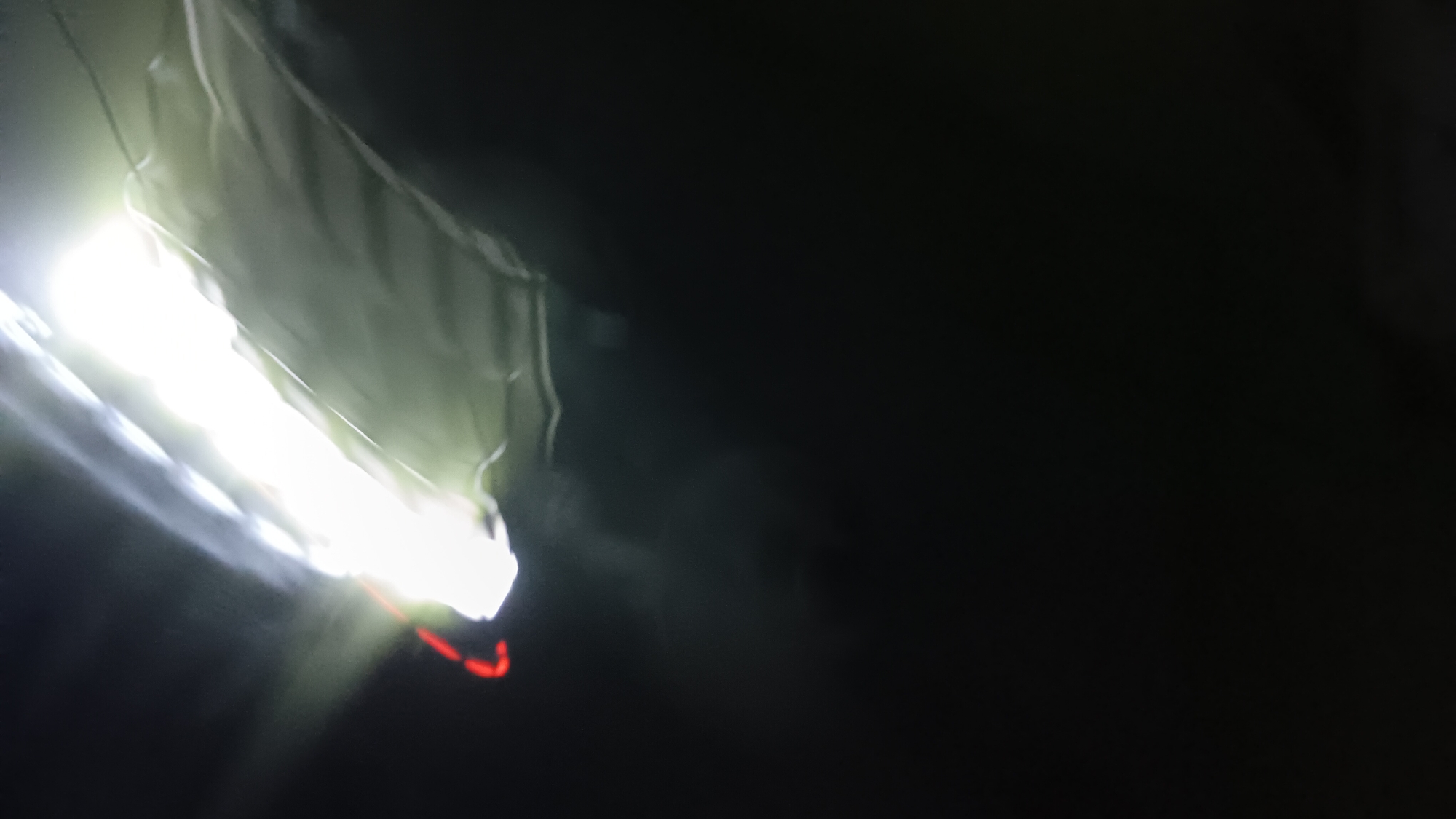 A highly blurred, low-light image captures what appears to be a bright light source illuminating a rippled, light-colored surface, possibly fabric, in the upper right quadrant. A thin red line is visible above the bright light. The rest of the image is dark and indistinct, with some subtle light diffusion. No specific landmarks or recognizable features are discernible, making it impossible to ascertain the location within Sonobekel, Indonesia, or any details about people, actions, or interactions. The image's quality prevents any forensic analysis or identification of specific objects or the environment.