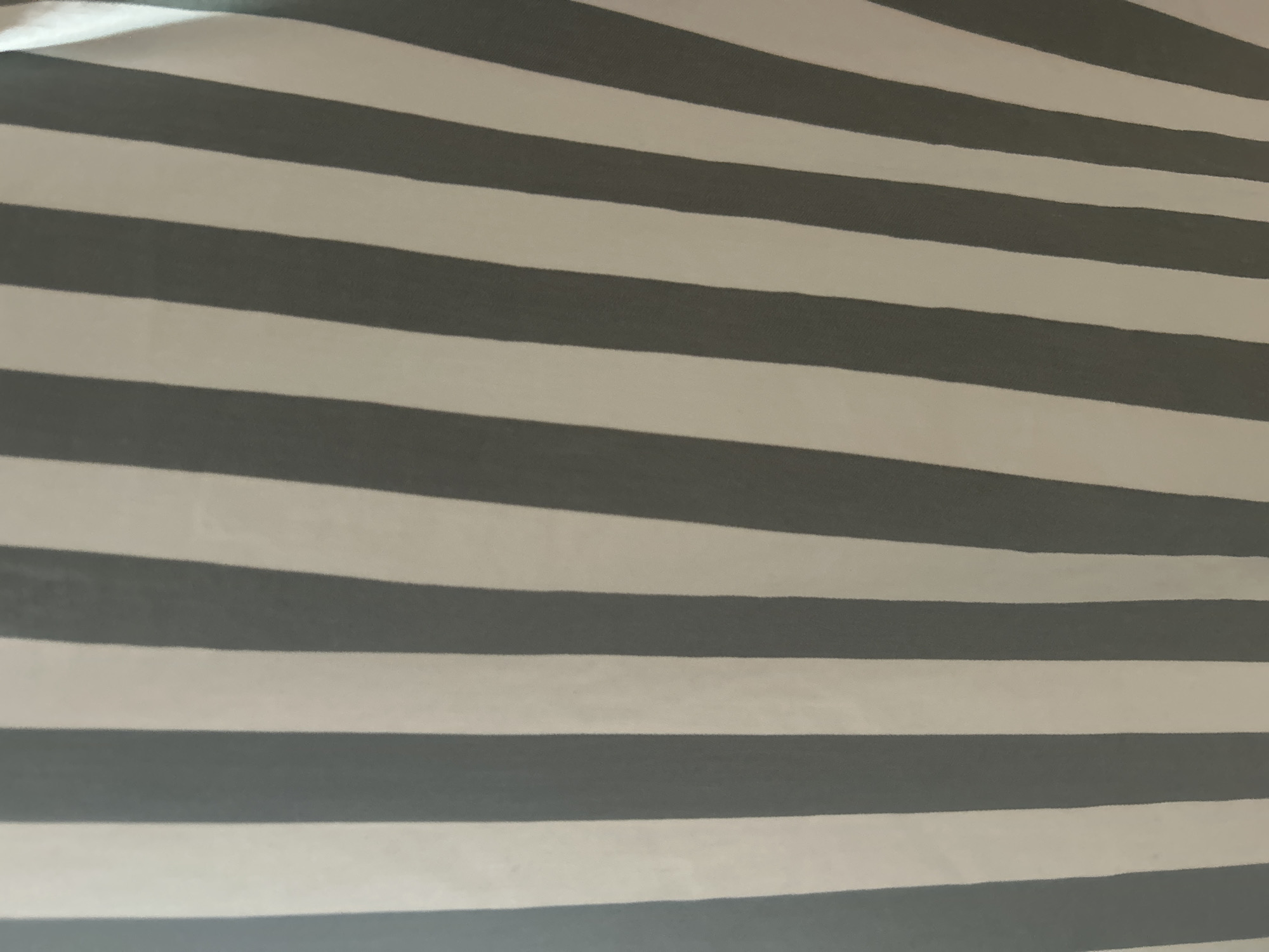 This is a close-up, abstract image of a striped fabric. The stripes are vertical and alternate between a dark gray and a white or off-white color. The fabric appears to be draped, as indicated by subtle folds and variations in lighting. There are no people, identifiable objects, or environmental context visible. The image provides no information that could be used to determine its location in Moscow, Russia, or any other specific geographic area.