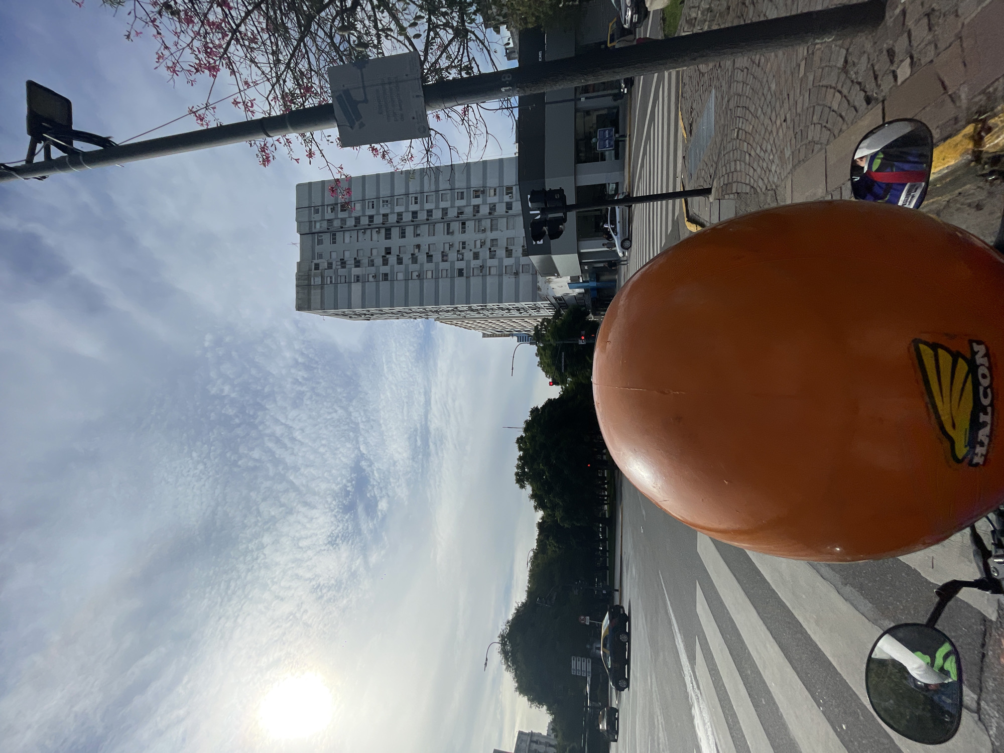 View from a motorcycle on a zebra crossing in Buenos Aires, Argentina. Tall building in the background. The sky is light blue with patterned clouds.