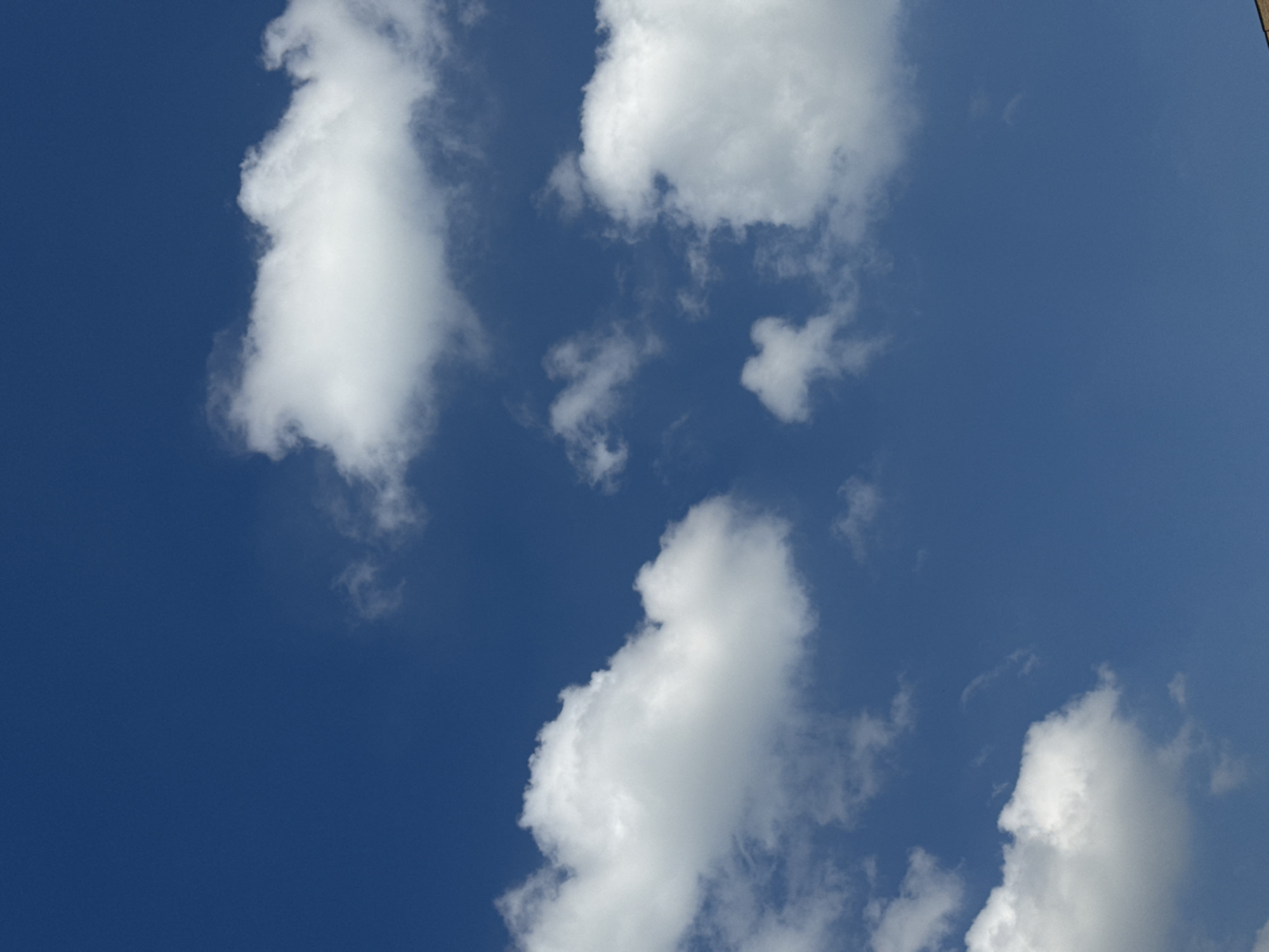 The image shows a blue sky with several white clouds. The clouds vary in size and shape, with some appearing larger and more defined than others. A building is located at the very top right of the image. The location is identified as Moscow, Russia. There are no people or interactions visible in the image.