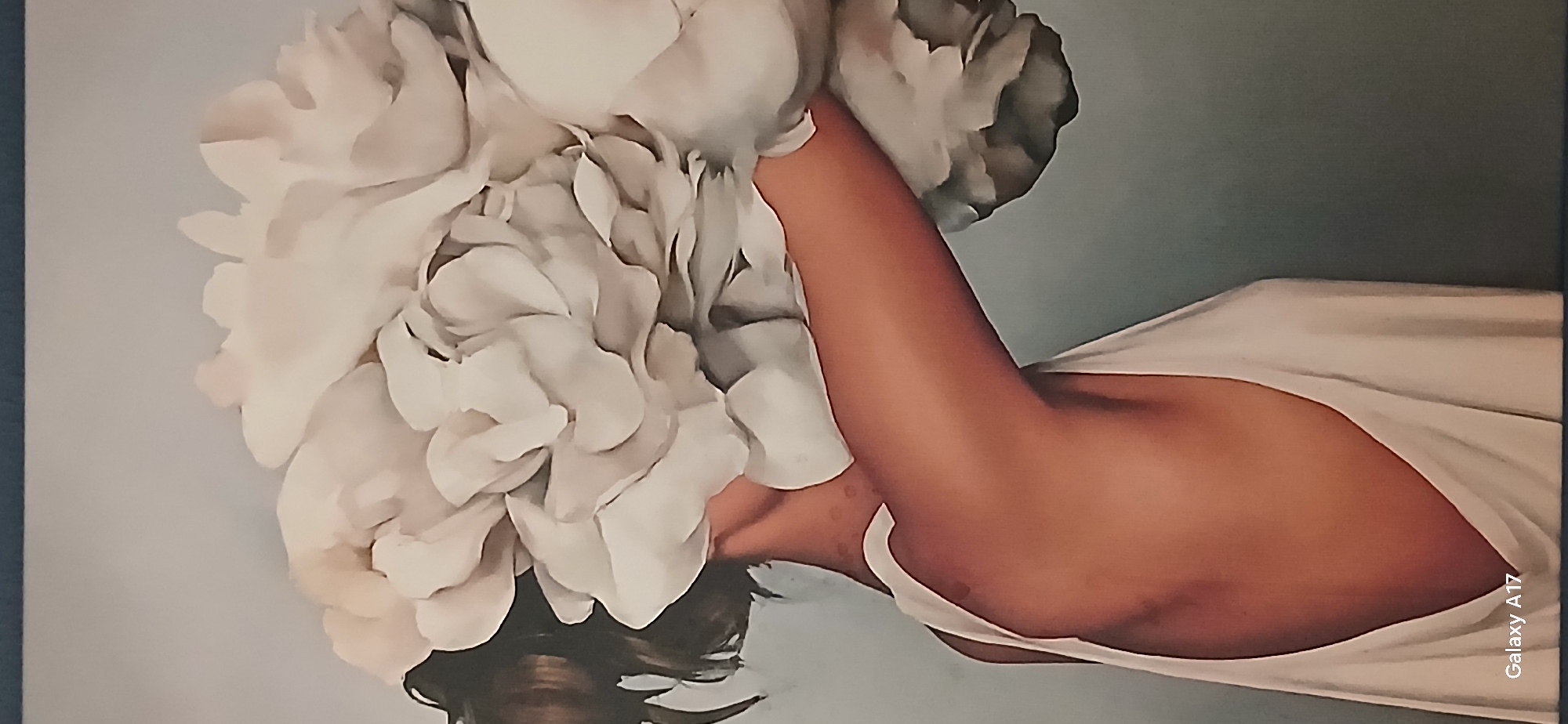 The image depicts a painting or print featuring a woman with a large, voluminous white flower arrangement partially obscuring her face. The woman is wearing a white dress or top, revealing a portion of her shoulder and upper chest. The background is a solid, muted gray-blue color.
Without additional information, it is impossible to determine if the image is located in Yekaterinburg, Russia.