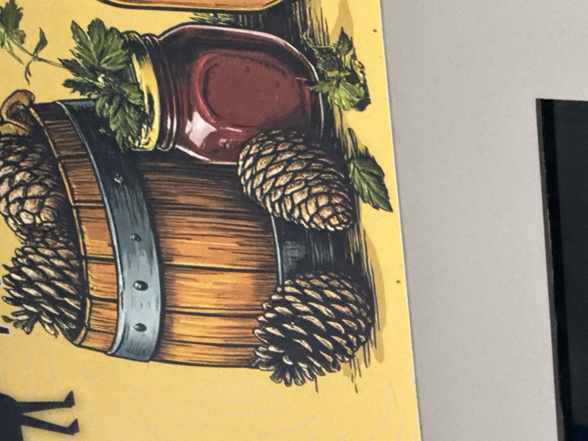 The image displays a close-up of a rustic still life painting featuring a wooden barrel filled with pinecones. To the right of the barrel is a glass jar containing a dark red substance, possibly jam or preserves, with a sprig of parsley or similar herb emerging from the top. Two pinecones are placed on a yellow surface in front of the barrel. A dark silhouette of what appears to be legs and feet is visible in the upper left corner of the frame. The overall aesthetic suggests a theme of nature or harvest. There is no discernible information within the image that would indicate its location in Norilsk, Russia.