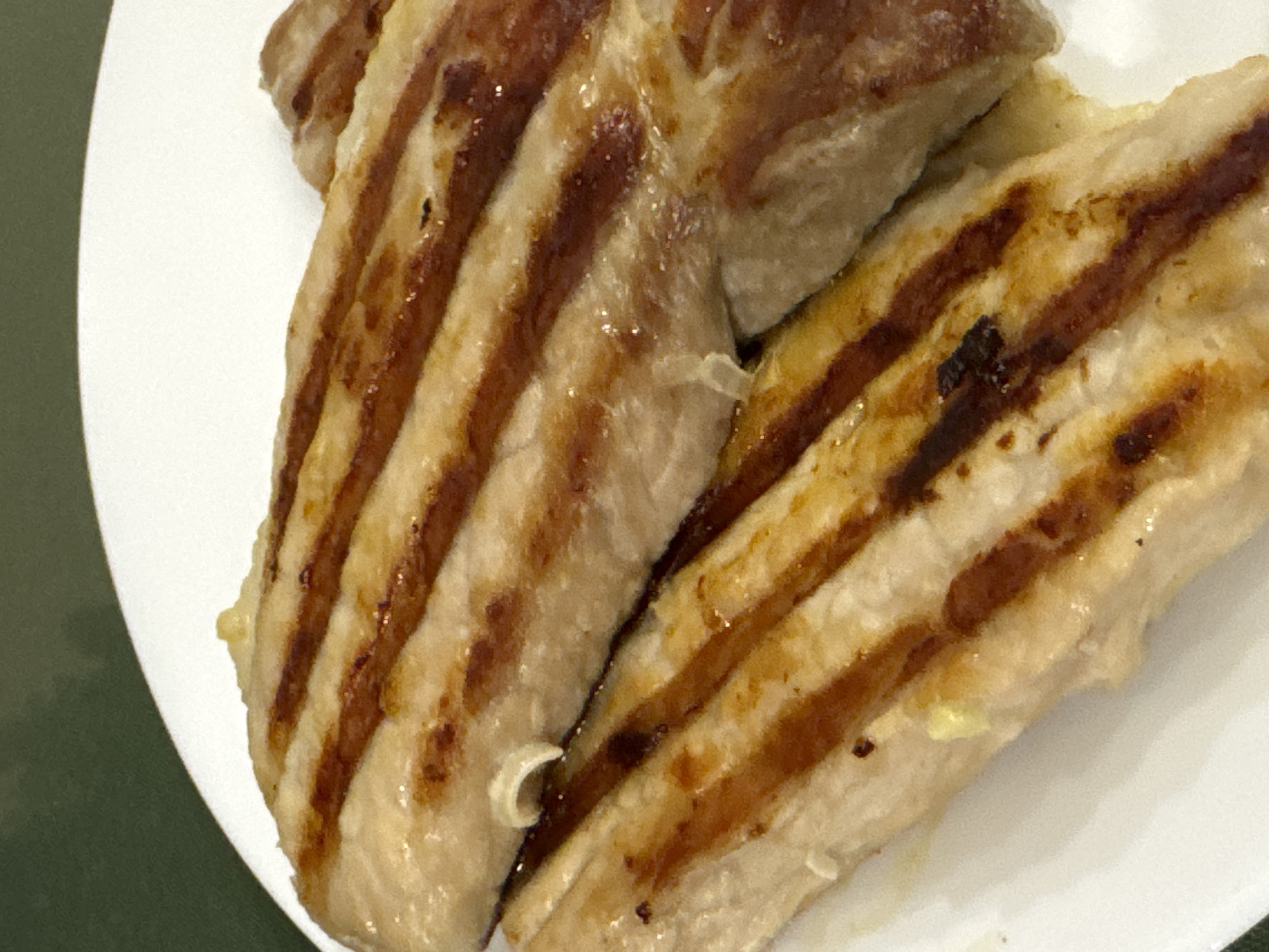 A close-up shows two pieces of grilled meat on a white plate. The meat has prominent grill marks and appears cooked. Part of the plate and a green surface are visible in the periphery. The city of Votkinsk, Russia, is not identifiable from the image. No people, actions, or interactions are visible.