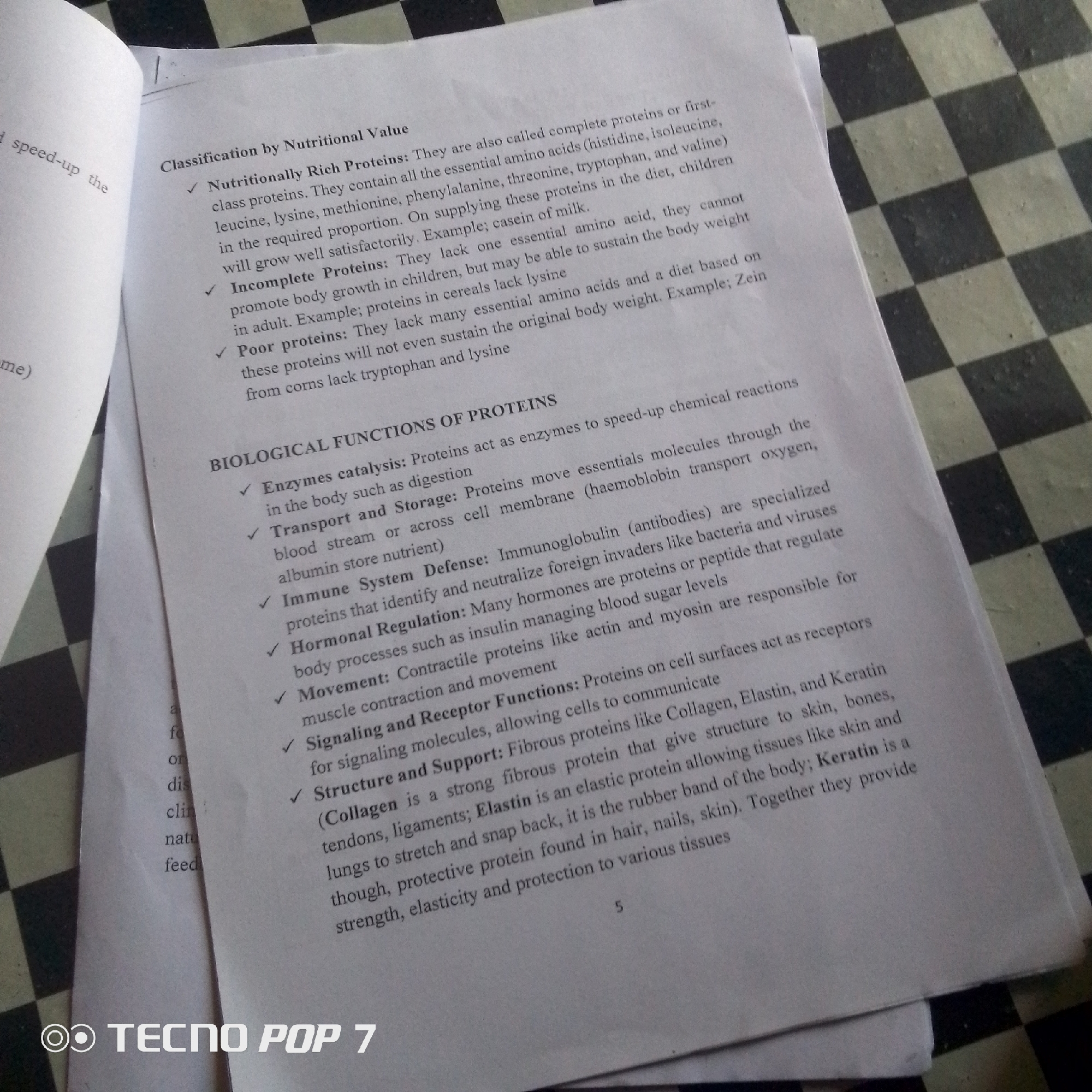 This media file is a close-up, slightly angled photograph of an open textbook lying on a black and white checkered surface. The textbook is white with printed text in black ink. The checkered surface appears to be a table or floor.
The textbook discusses proteins, categorizing them by nutritional value (Nutritionally Rich, Incomplete, and Poor proteins) and then by their biological functions (Enzymes catalysis, Transport and Storage, Immune System Defense, Hormonal Regulation, Movement, Signaling and Receptor Functions, and Structure and Support). There are several bullet points with checkmarks indicating different categories and examples. The page number "5" is visible at the bottom right of the textbook.
A portion of another page or object is visible on the left side of the image, showing some text including "speed-up the" and "me)". In the bottom left corner of the image, a watermark reads "TECNO POP 7".
The lighting suggests it might be daytime, possibly indoors with artificial lighting, given the absence of strong shadows. The scene is static and educational, focusing entirely on the content of the textbook and its immediate surroundings. There are no people visible in the image, and the emotions conveyed are neutral, related to the academic subject matter. The location is hinted at by the watermark, suggesting it was taken with a Tecno Pop 7 phone. There are no specific Jalingo, Nigeria location cues visible within the image itself, other than what might be inferred from the phone model.