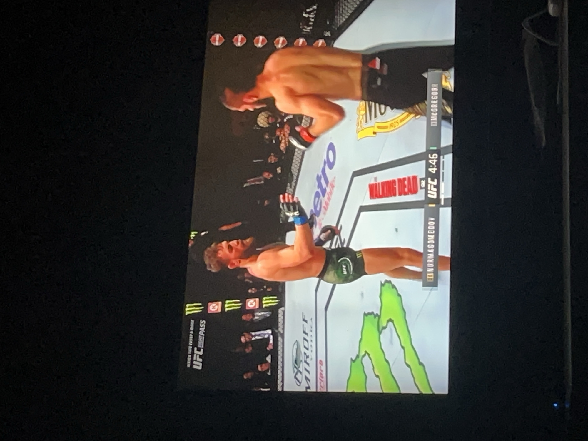 The image shows a television screen displaying a UFC (Ultimate Fighting Championship) match. Two fighters are in the ring; one with green shorts and the other with black shorts. The UFC logo and the words "Walking Dead" are visible in the image. The city of Yerevan, Armenia is not evident in the provided image or any associated details.