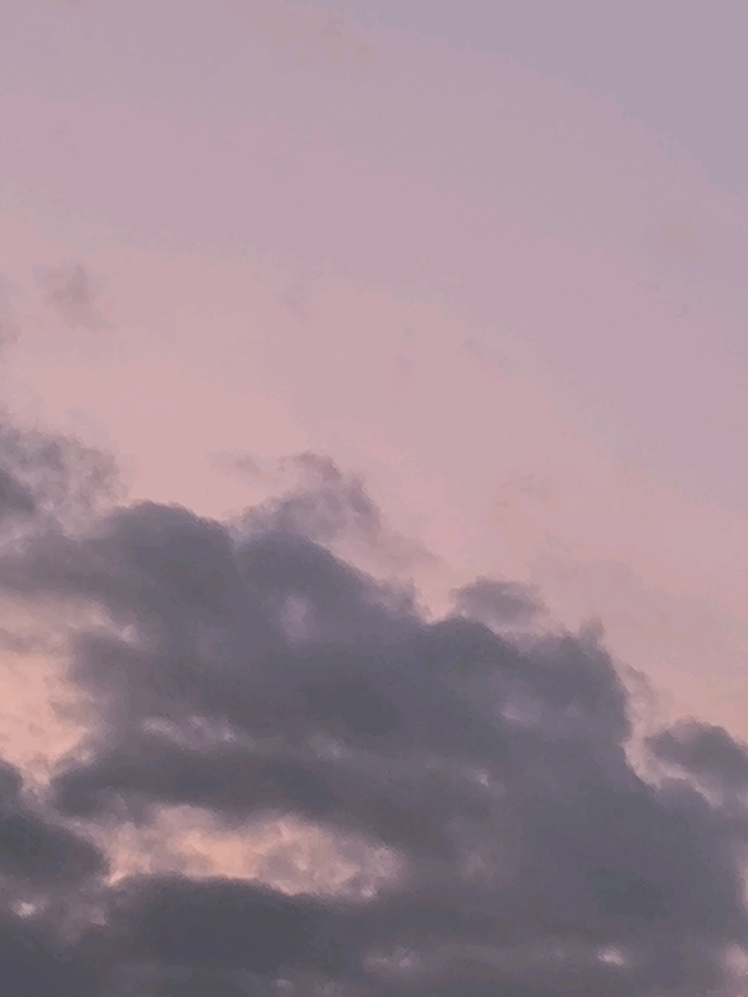 The image depicts a painterly depiction of a dusky sky with clouds. The upper portion of the image is a soft, gradient of pale pink and lavender, suggesting a sunset or sunrise. Below this, darker, more textured clouds are rendered in shades of deep purple, grey, and muted pink. The style is reminiscent of an oil painting, with visible brushstrokes creating a soft, atmospheric effect. The scene is devoid of any discernible landmarks or elements that would indicate a specific location within a city.