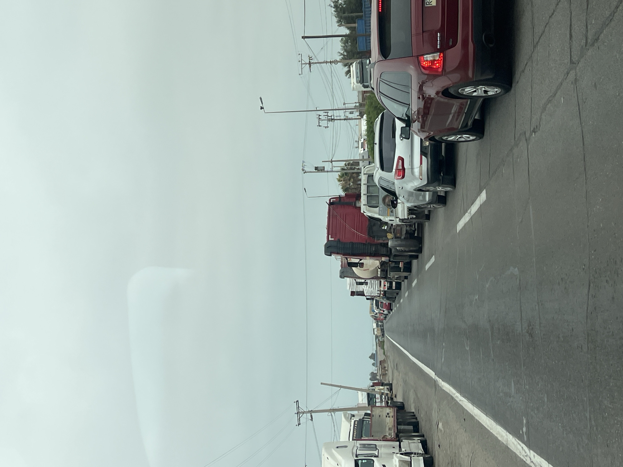 The image shows a traffic jam on a road in Arica, Chile. A line of cars and trucks stretches into the distance. The sky is overcast. Utility poles line the road.