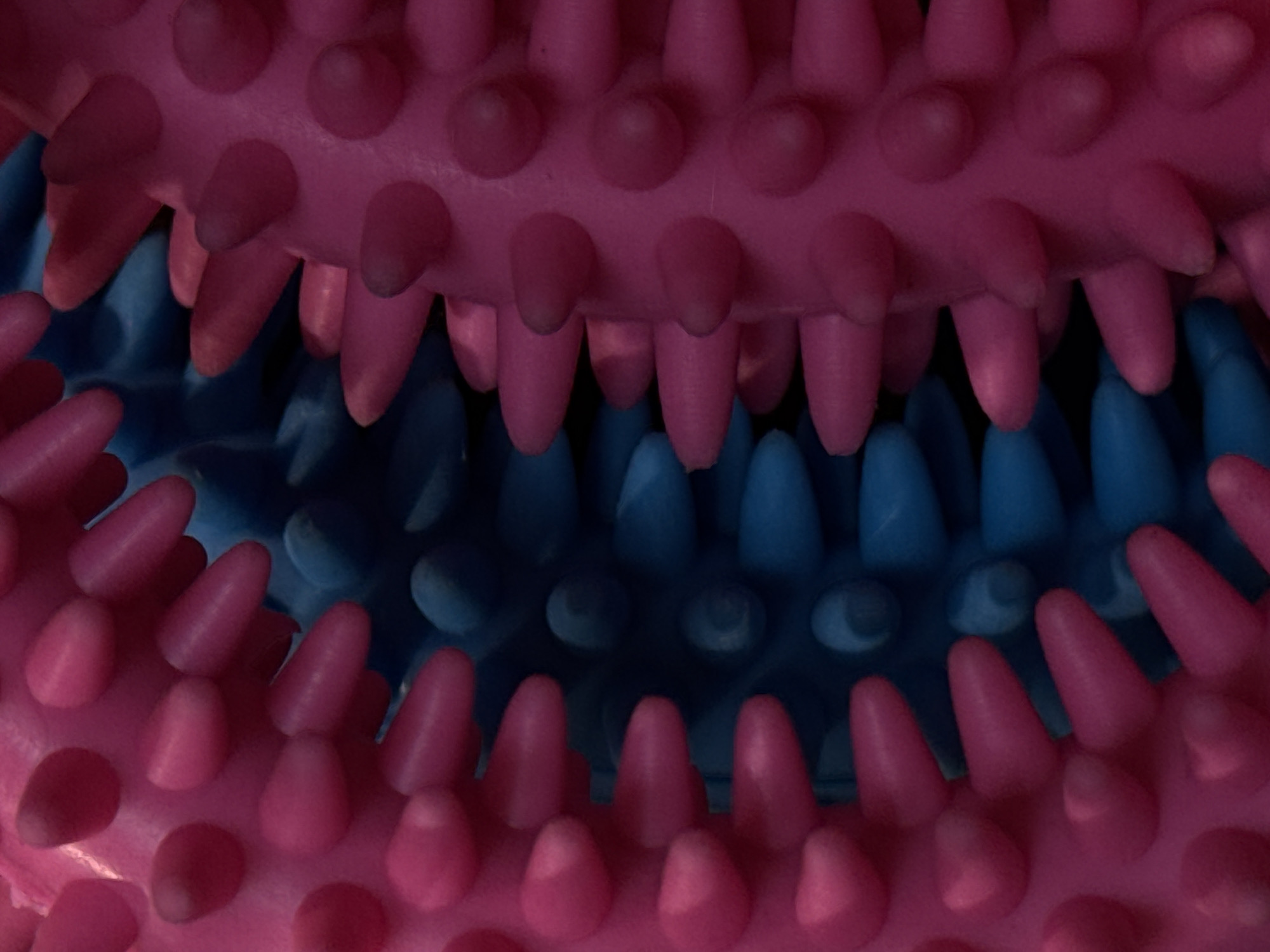 The image is a close-up, abstract photograph of two spiky massage balls, one pink and one blue, positioned next to each other. The texture of the rubber spikes is the primary focus, with the lighting creating a sense of depth and form. There are no discernible environmental features, buildings, or any indication of a specific location, including Moscow, Russia. The image solely depicts the tactile surfaces of the massage balls.