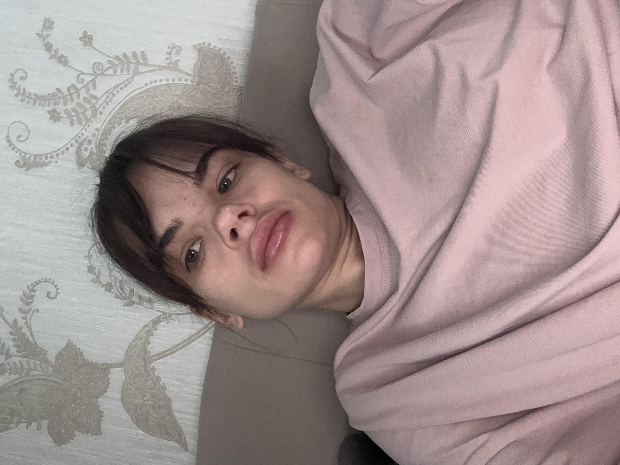 A woman with dark hair and bangs lies on a surface with a pale floral pattern. She is partially covered by a pink garment. The location is unknown and there is no indication of Rostov-on-Don, Russia.